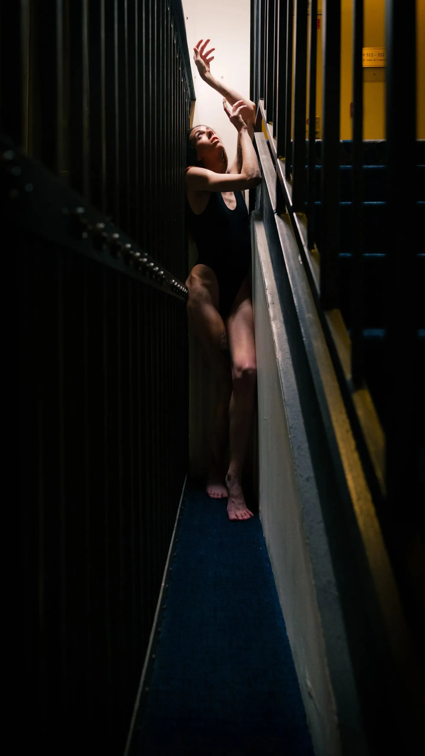 A figure catches warm window light through the bars of a stairwell.