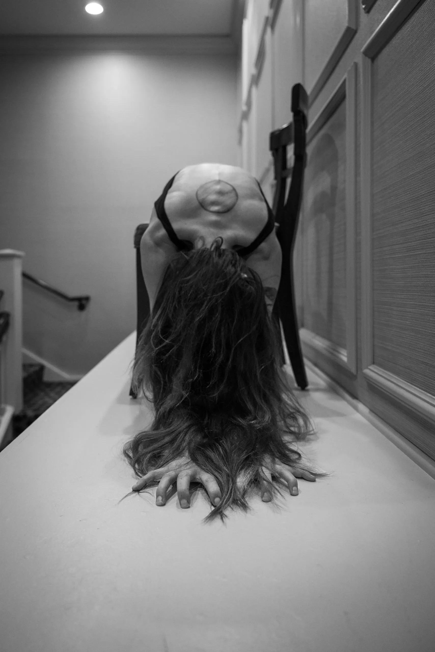 A woman lies prone over a chair along a corridor ledge with her hair spilling toward the camera.