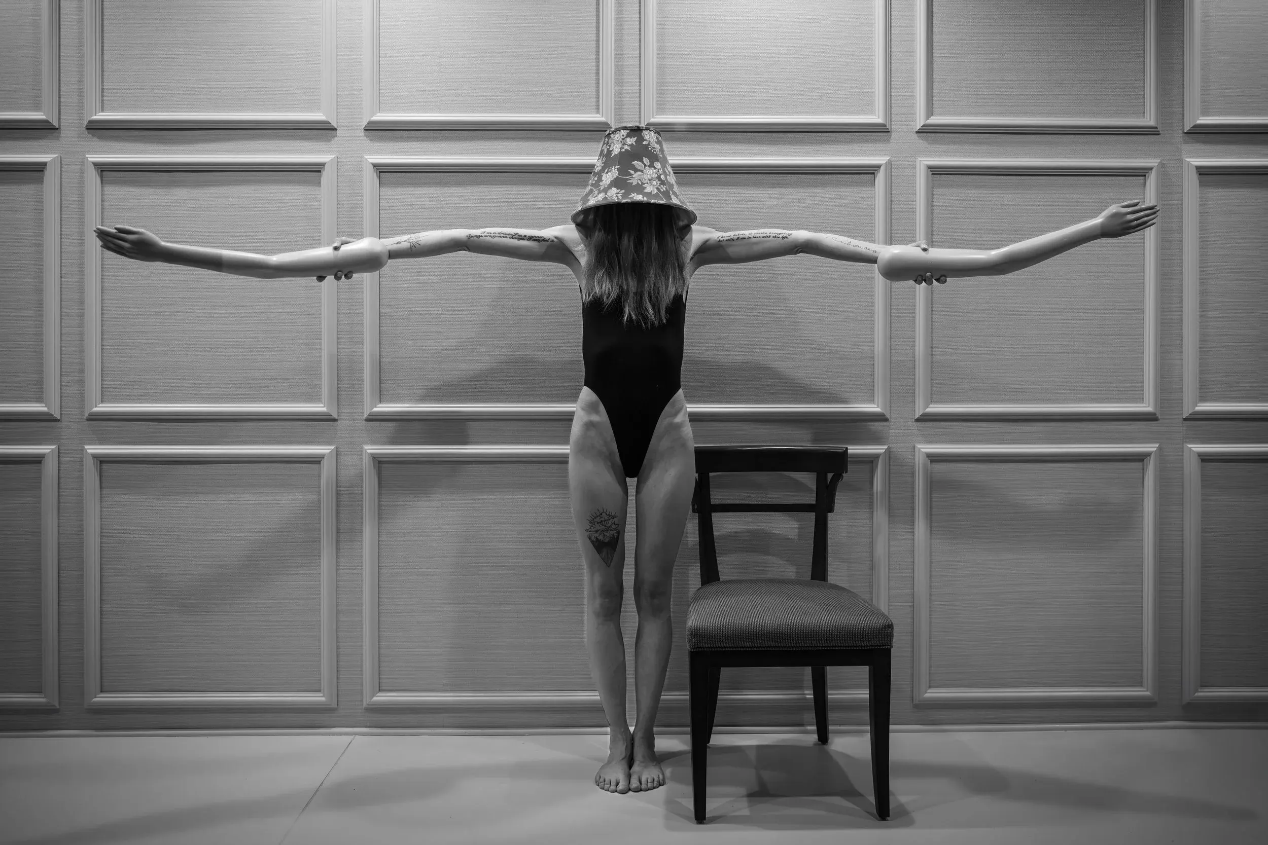 A woman wearing a lampshade on her head holds two mannequin arms, making her arms look extremely long.