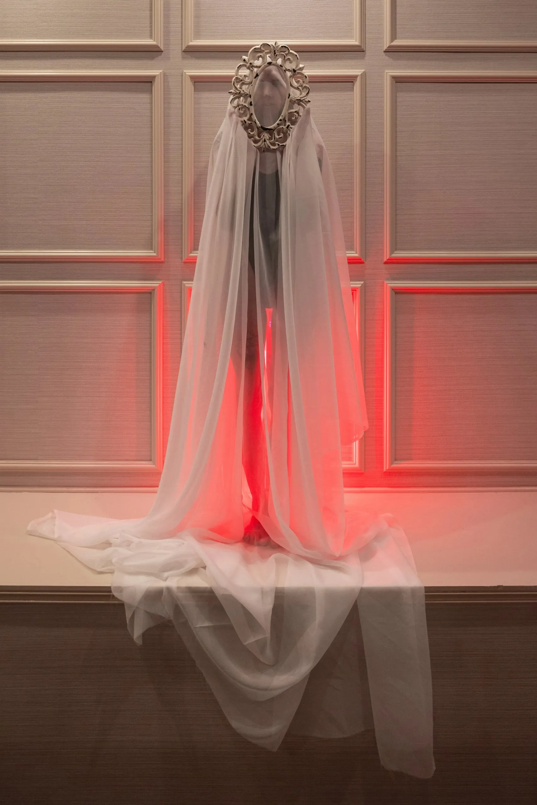 A ghostlike veiled figure glows red against pale wall panels.