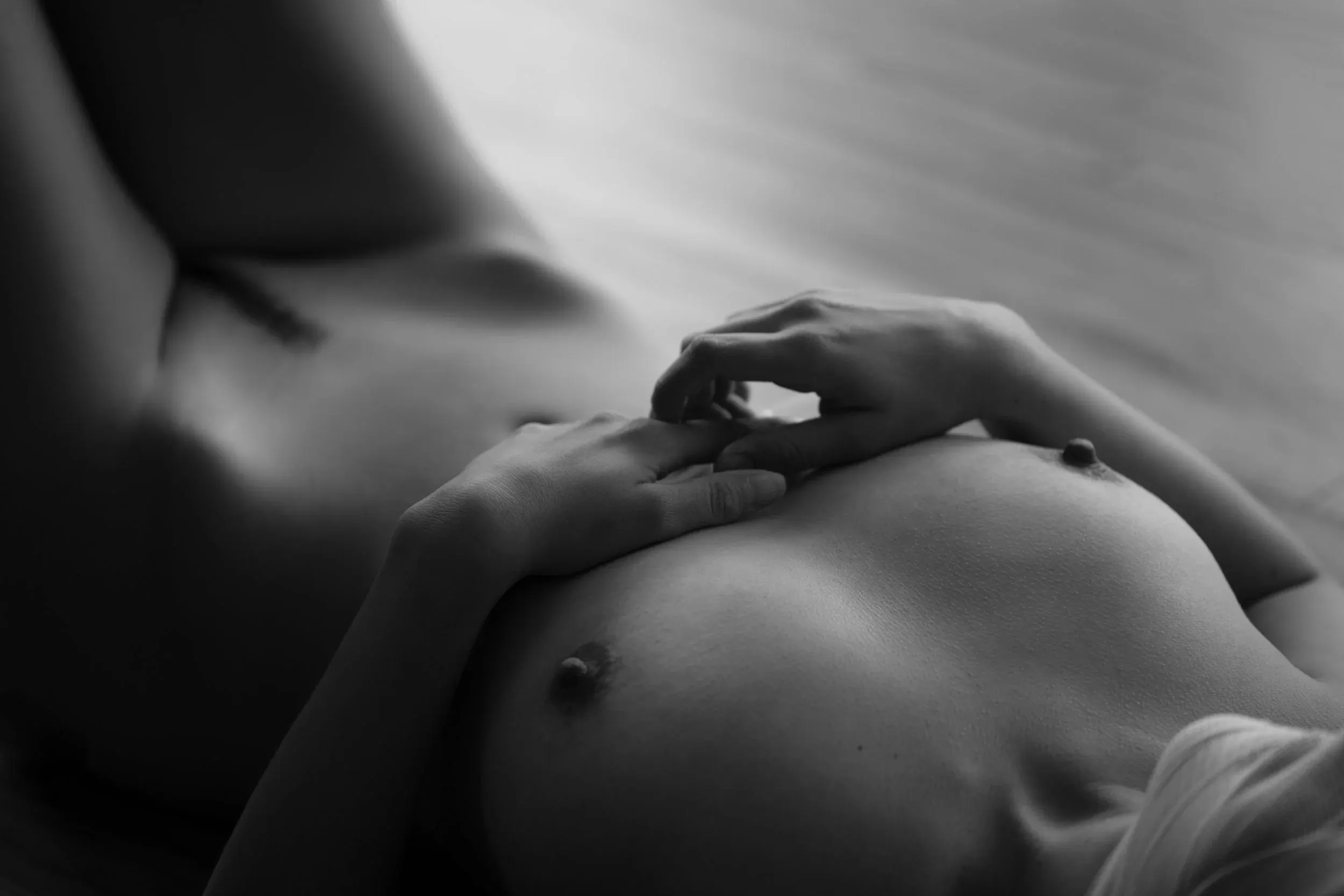 A nude woman lies on her back on the floor. Soft window light illuminates her body, and her head appears to be wrapped in bandages.
