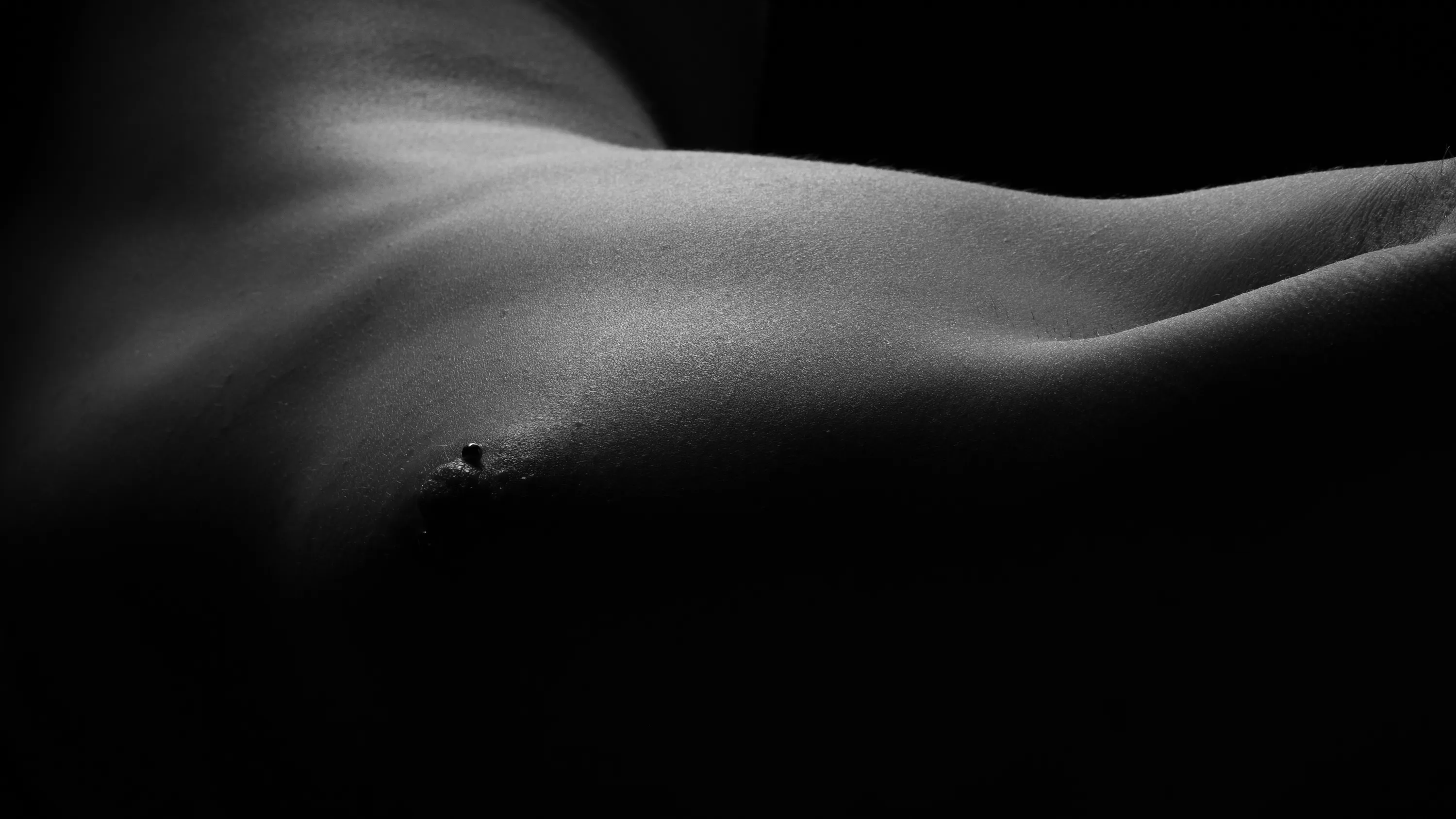 A subtle bodyscape, black and white, showing the contours of a woman's upper body as she lies on her side, toward the camera.