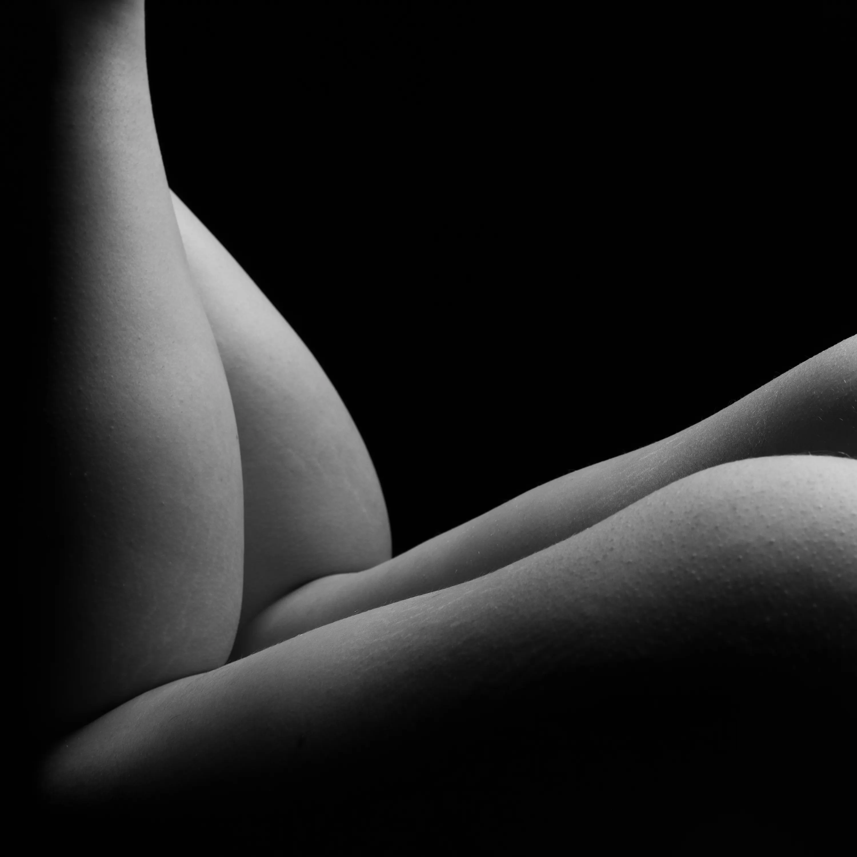 Close-up of the backs of a woman's bent legs, lit in a chiaroscuro style.