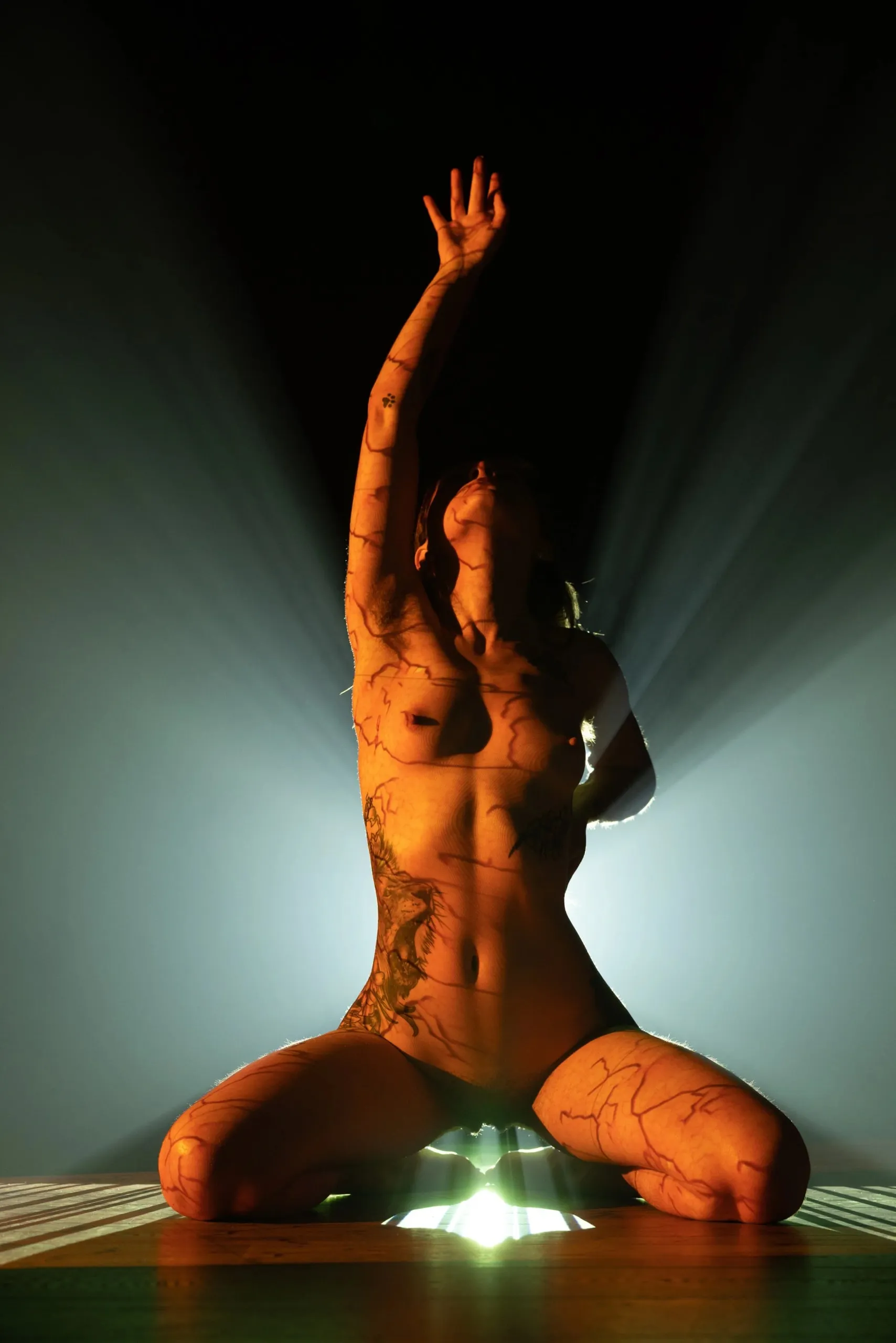 A kneeling woman raises one arm above the projector and radiant haze.
