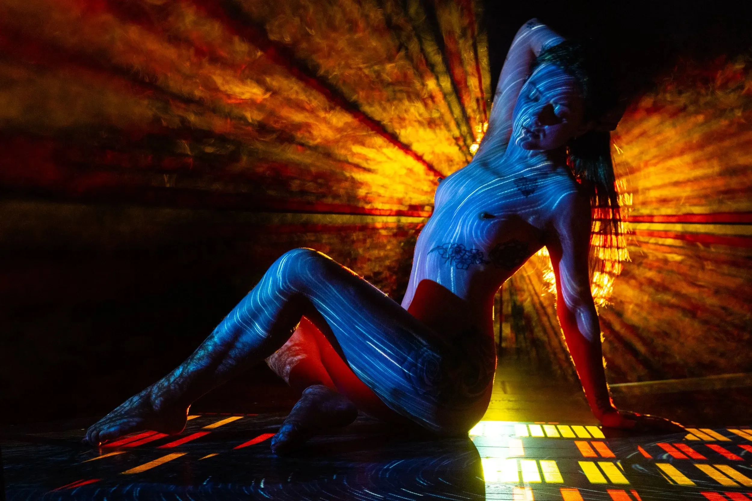 A seated woman glows blue before a fan of red and orange light.