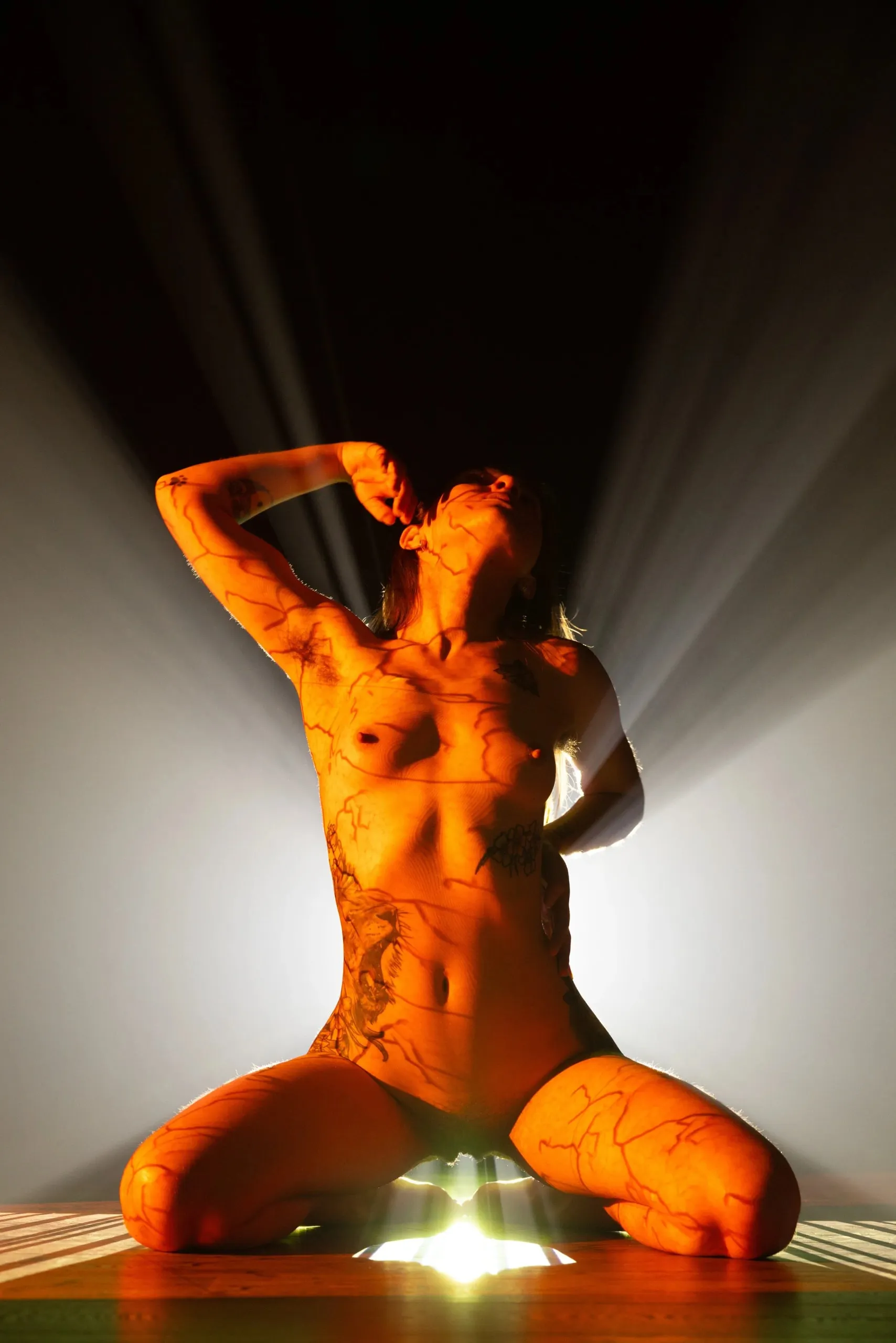 A kneeling woman raises one arm against strong white backlight.