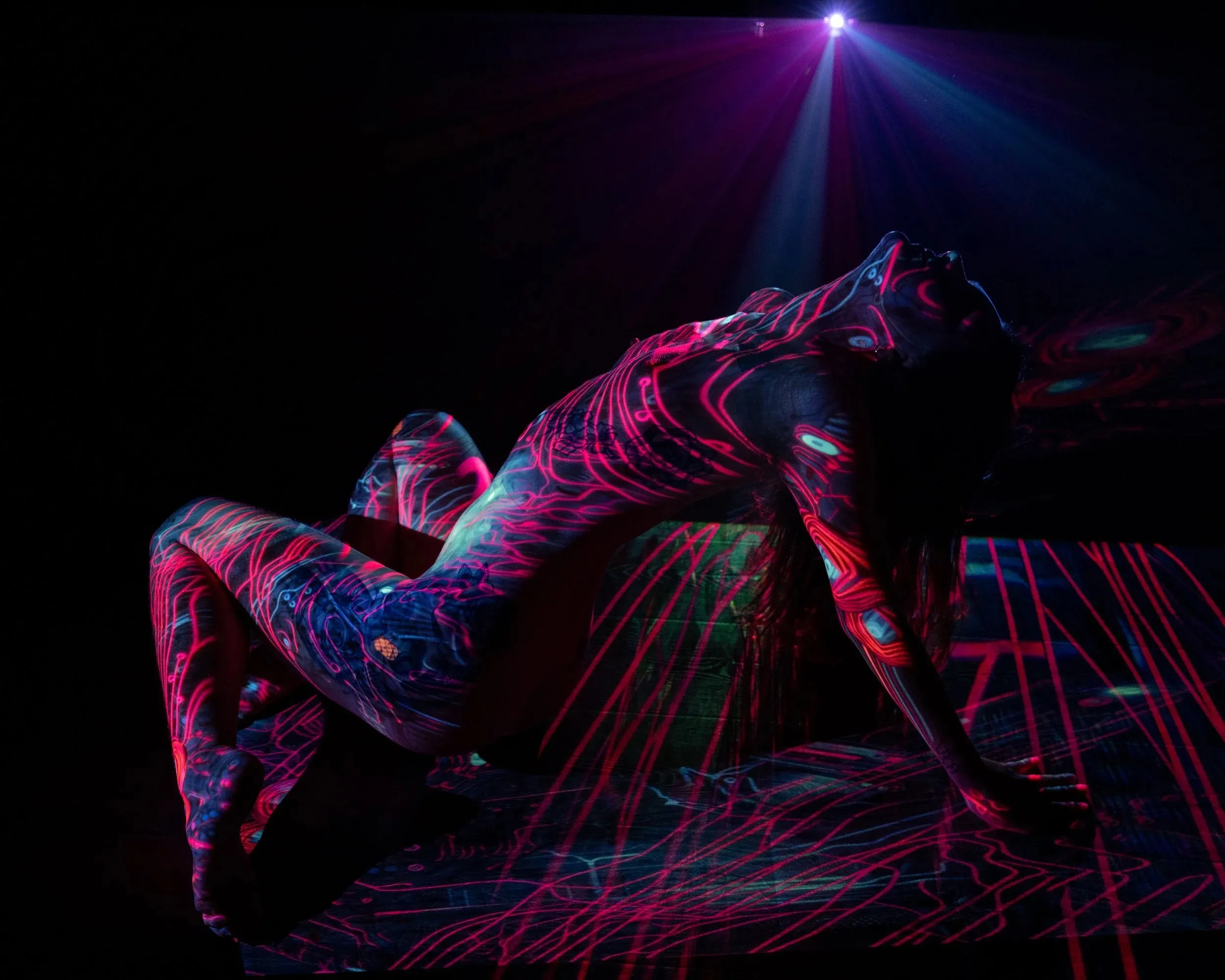 Red and blue projected lines cover a reclining figure beneath a violet beam.
