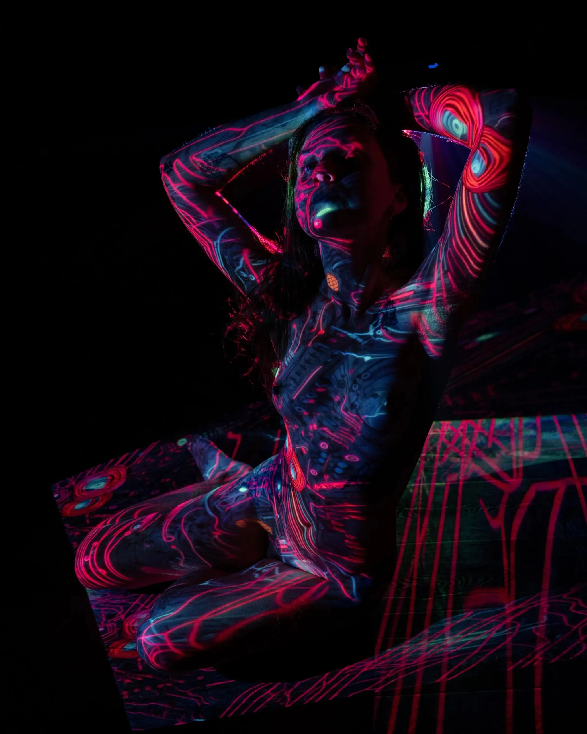 A seated woman lifts both hands through red and blue projected patterns.