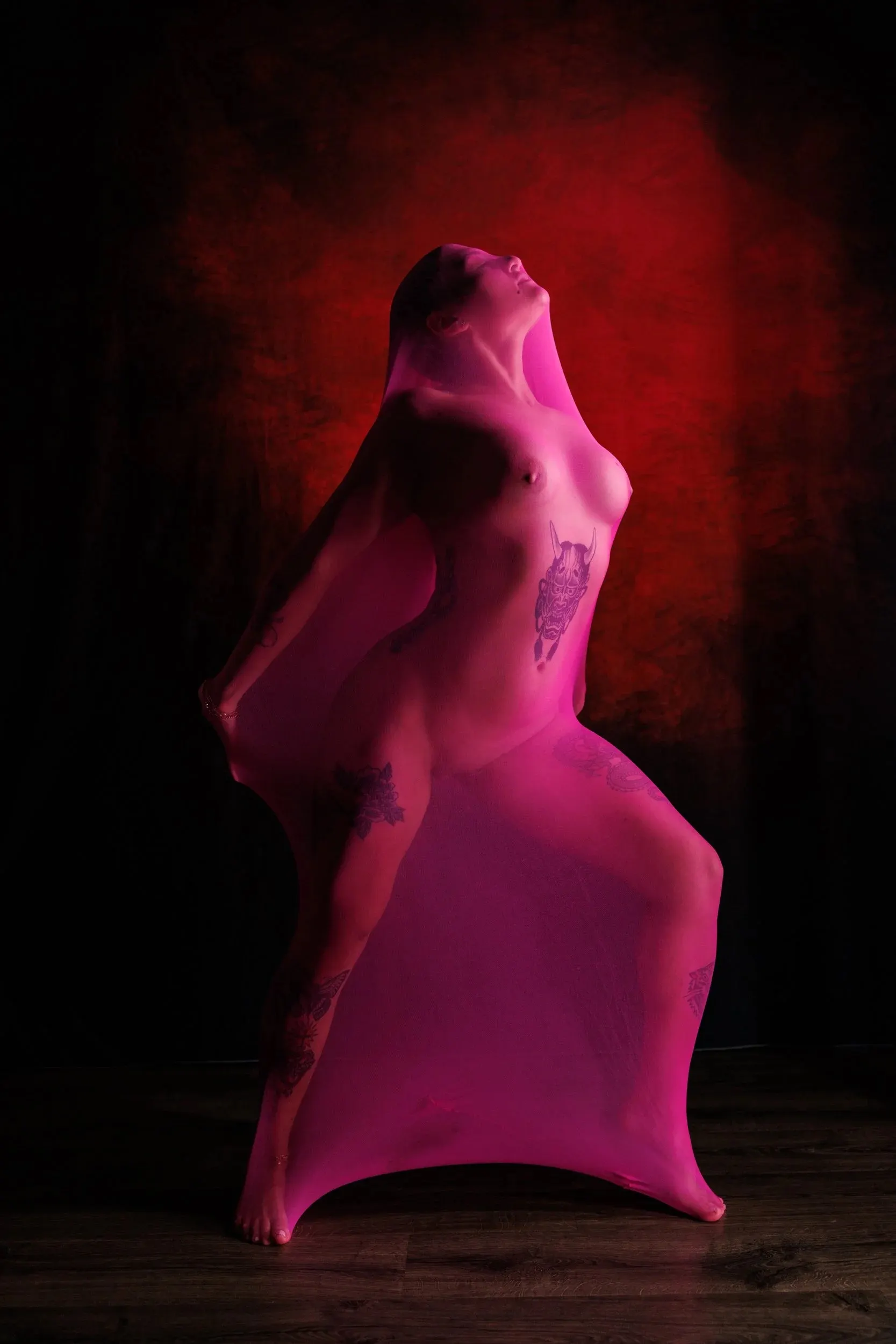 A woman stands, arching to the side and looking up, wrapped in a pink body cocoon.