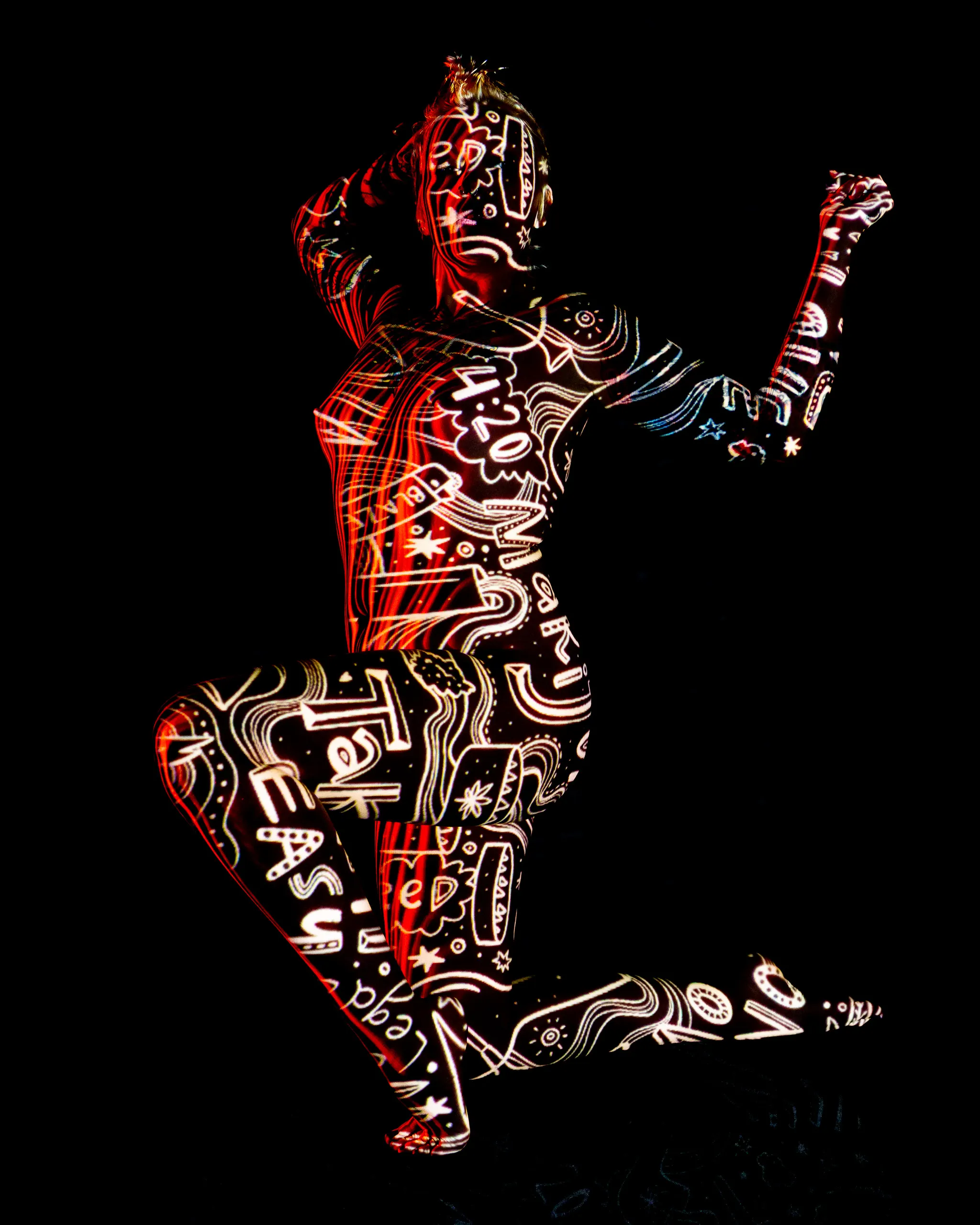 A woman crouched on one knee, dense red-and-white graffiti-style text and doodles projected across her whole body against black.