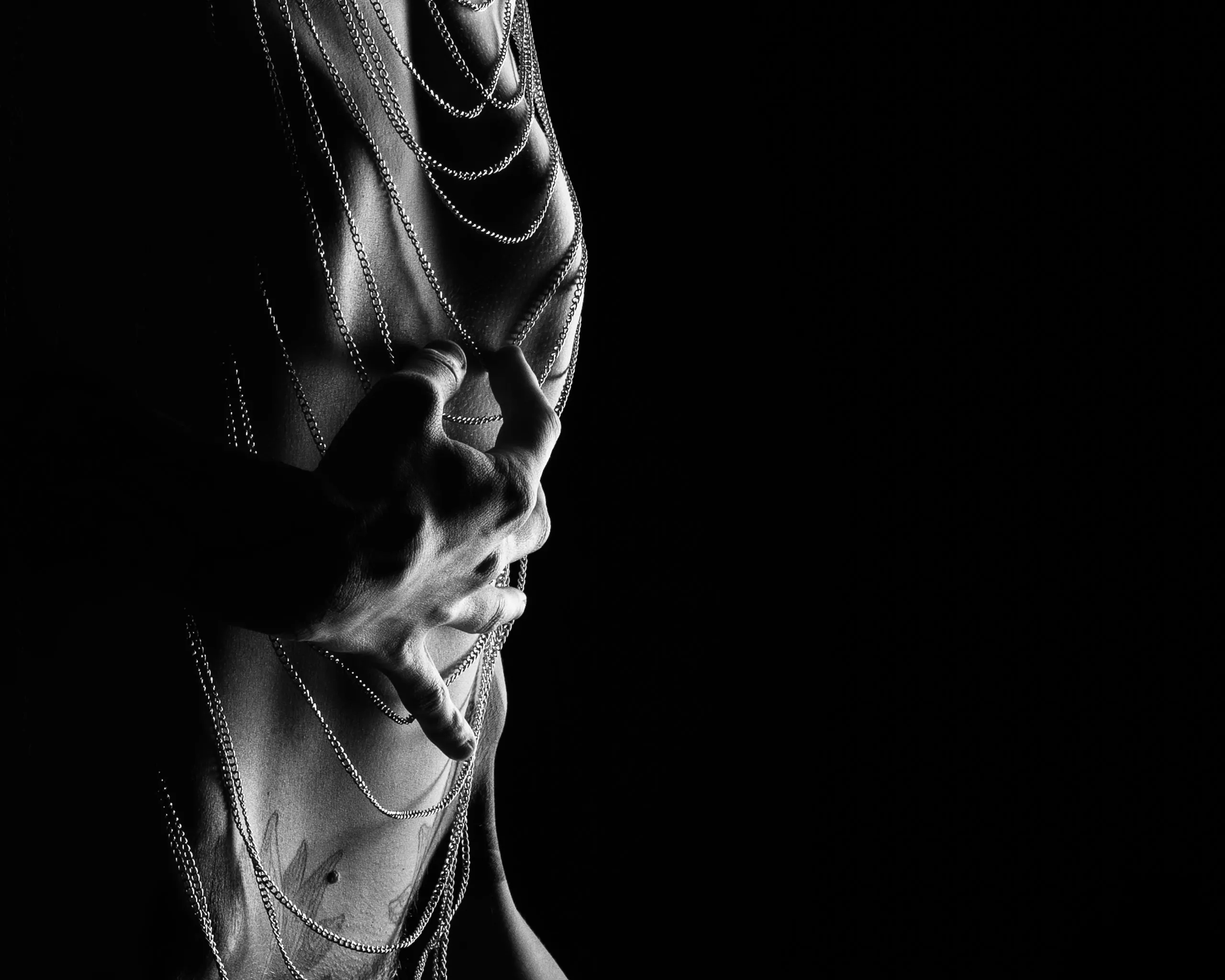 Hands gather strands of chain across a dramatically lit torso.