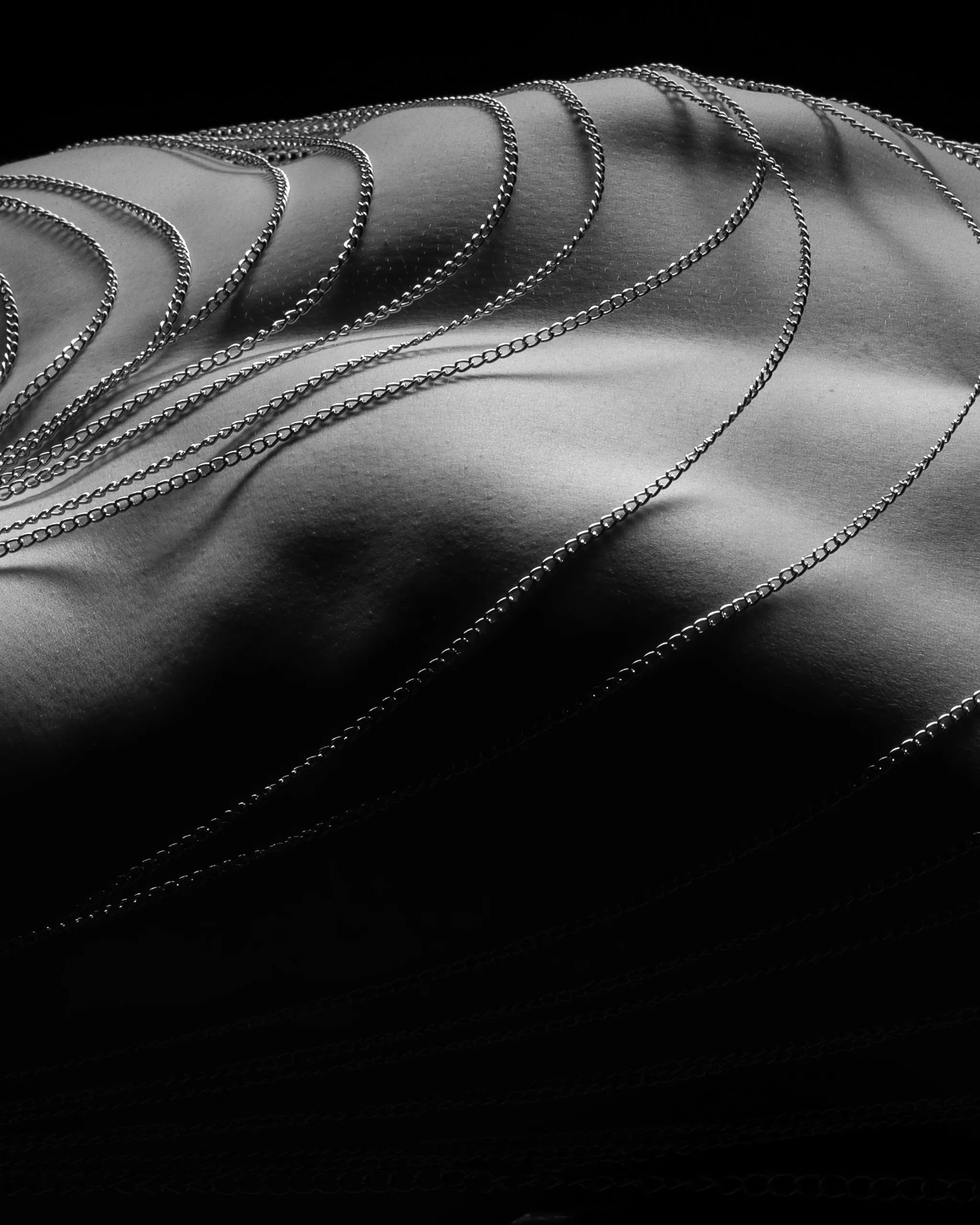 Chains trace the curves of a reclining figure in raking light.