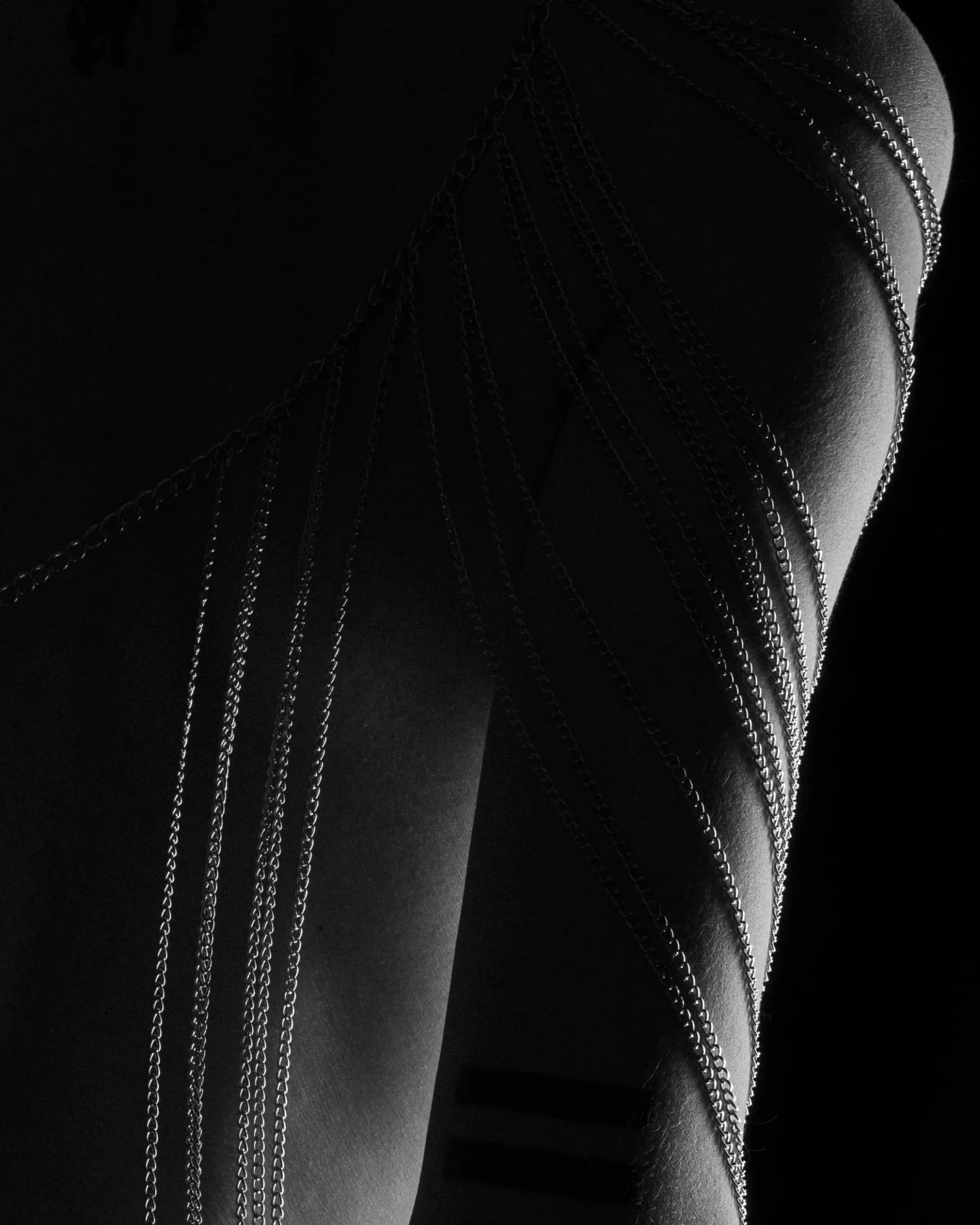 Parallel chains fall across a shadowed side in a vertical abstract study.