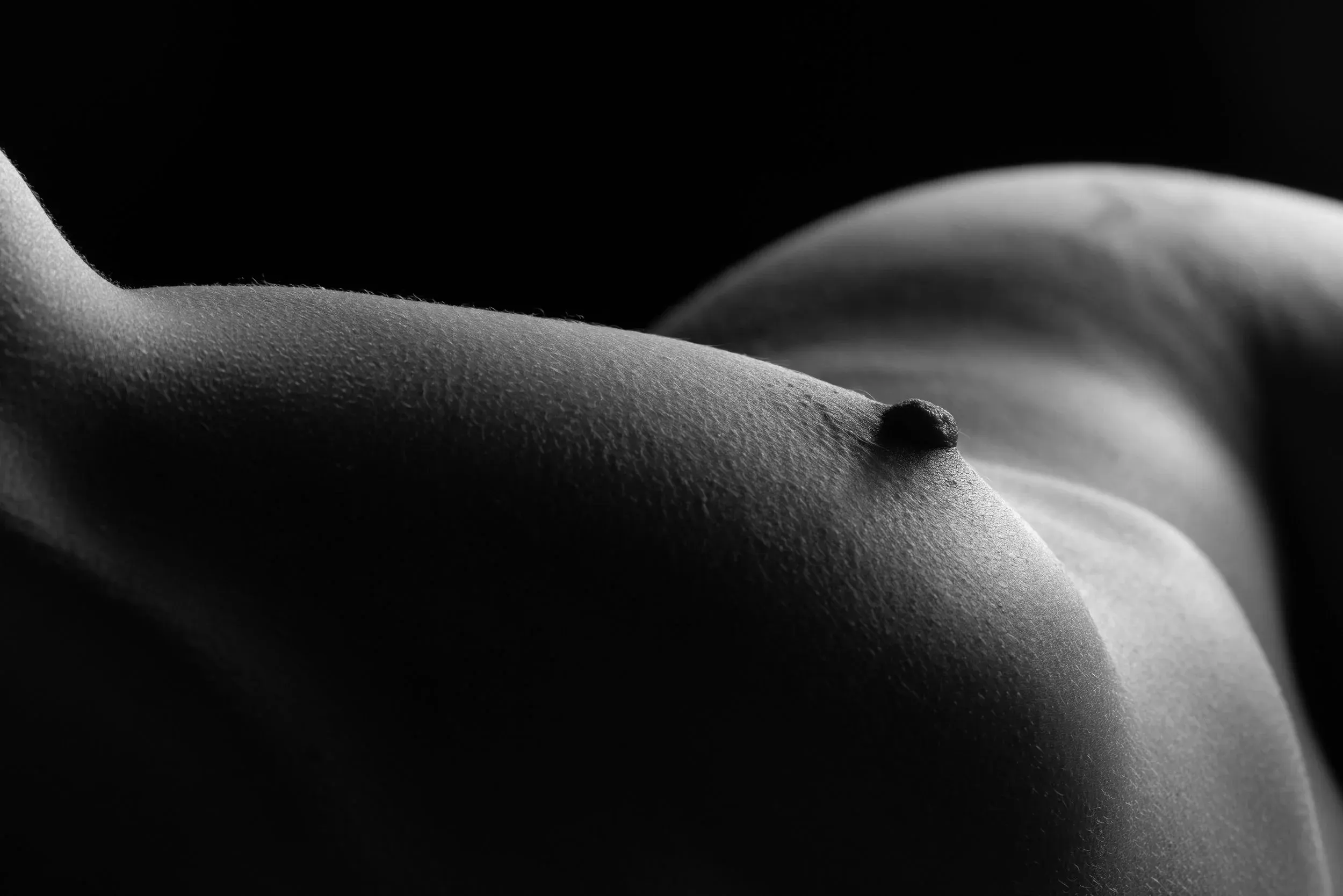 Close-up bodyscape of a woman's breast and hip in the distance.