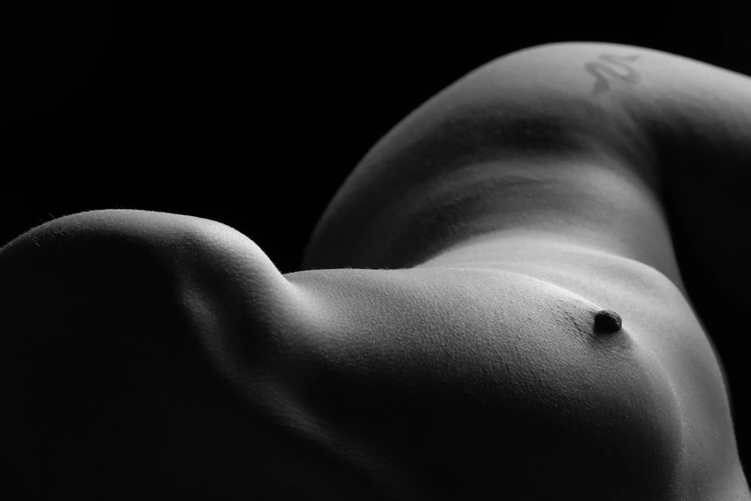 Close-up bodyscape of a woman's breast and hip in the distance.