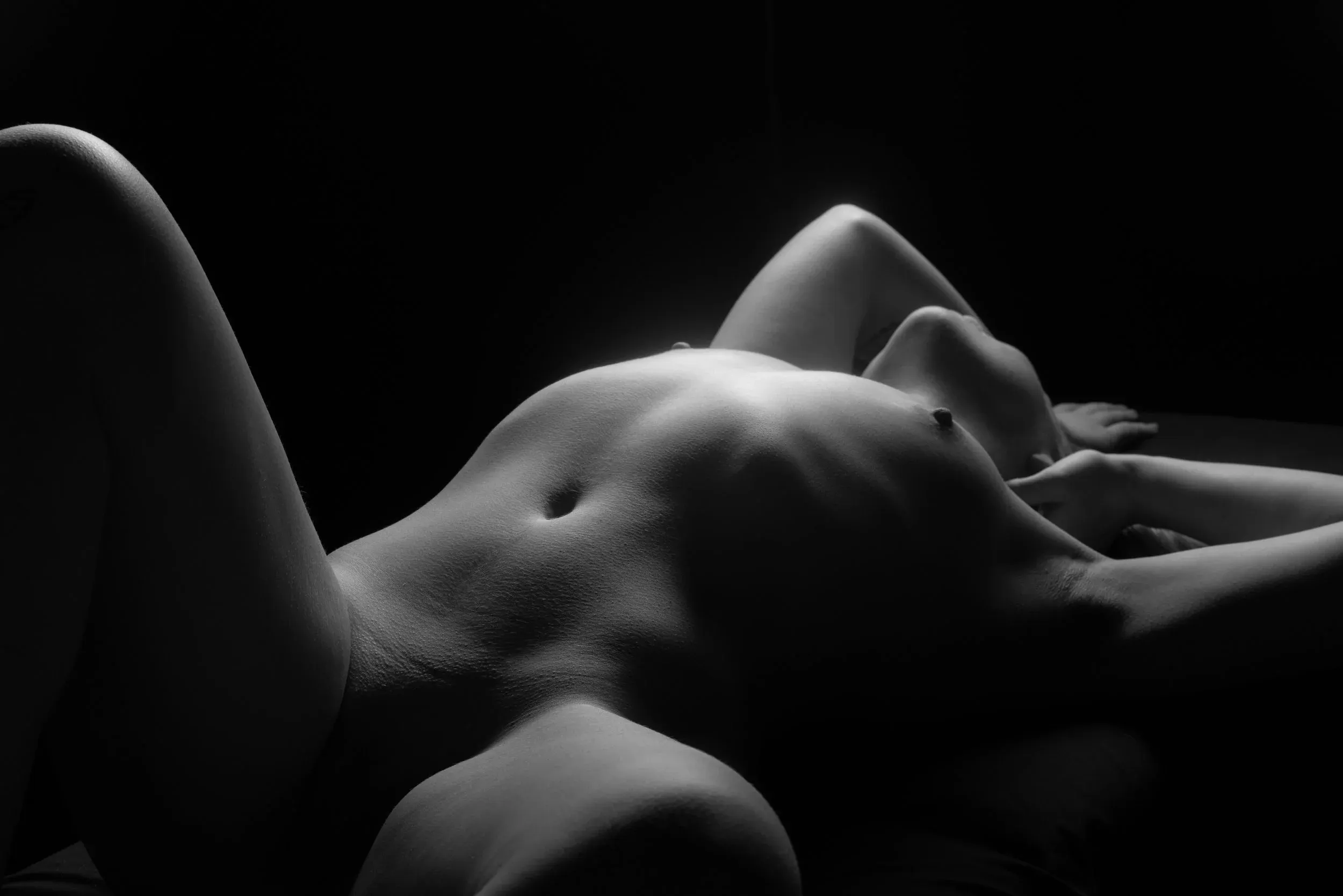 An erotic bodyscape view of a woman on her back, knees apart, shadows providing modesty.