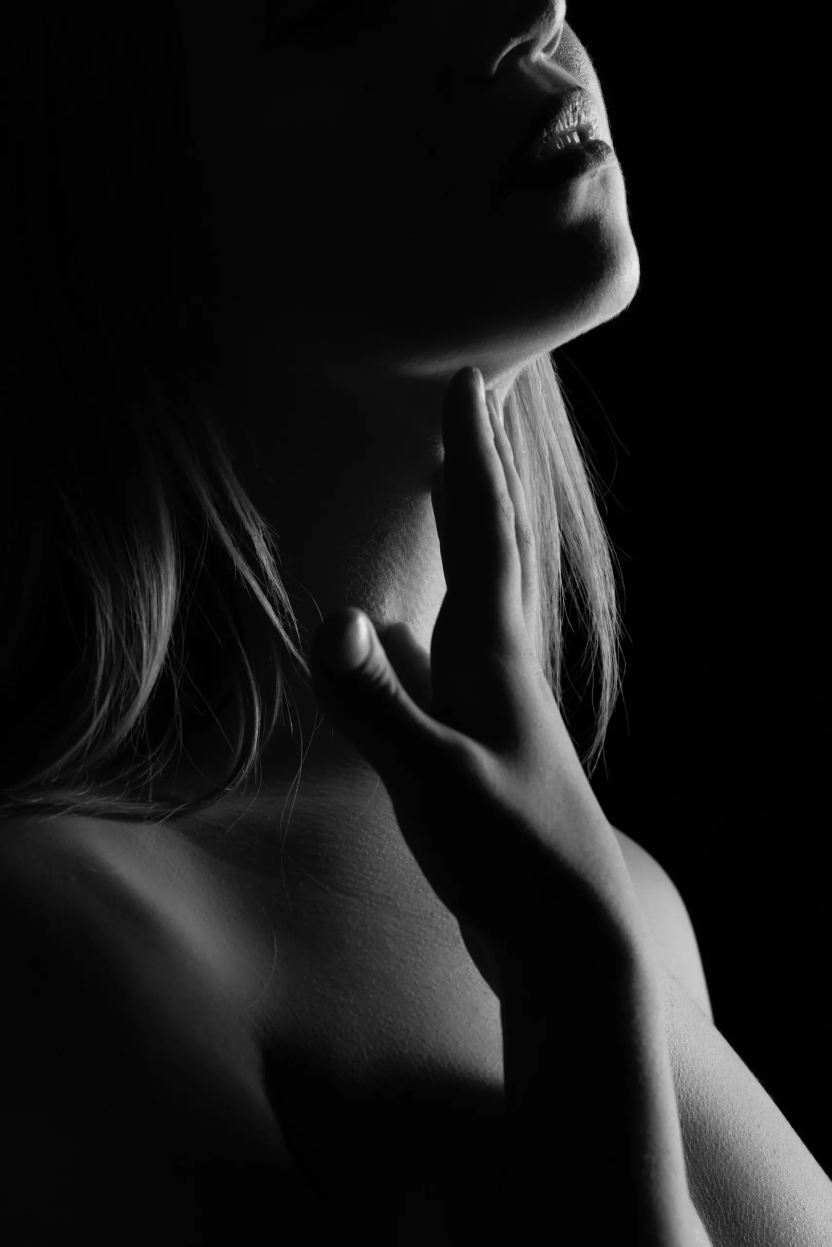 A close profile of chin and shoulder emerges from deep black.