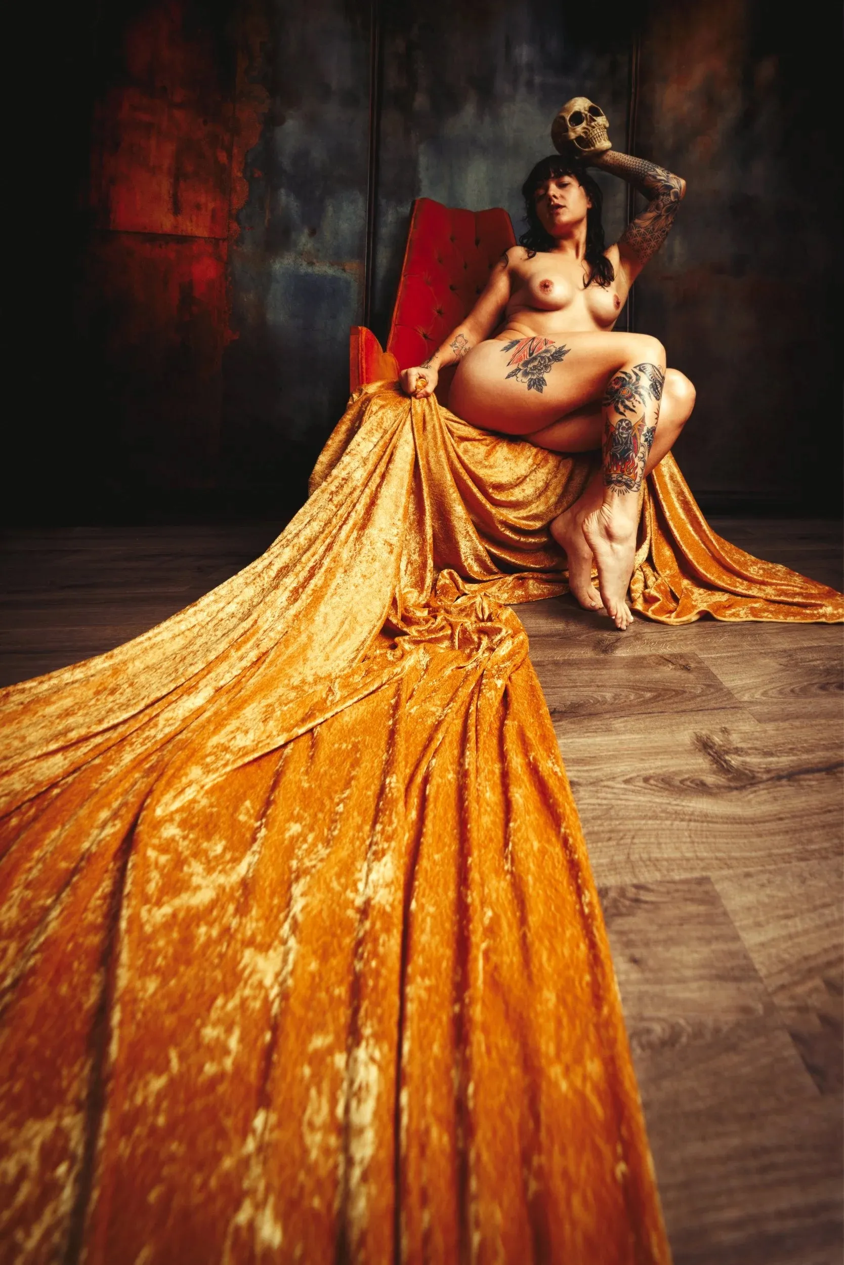 A nude, tattooed woman sits on a distant throne beyond a sweep of gold fabric.