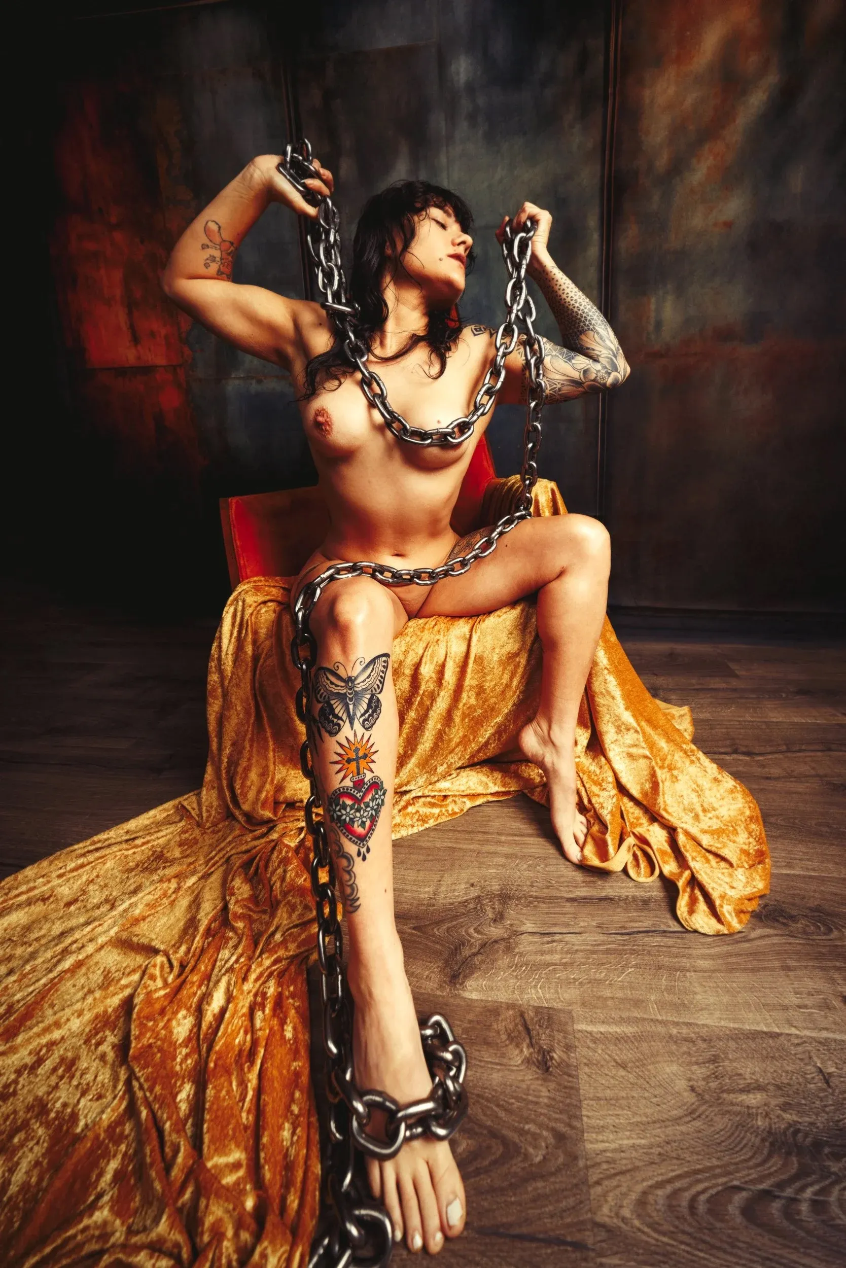 A seated woman lifts chains overhead amid red, gold, and black tones.