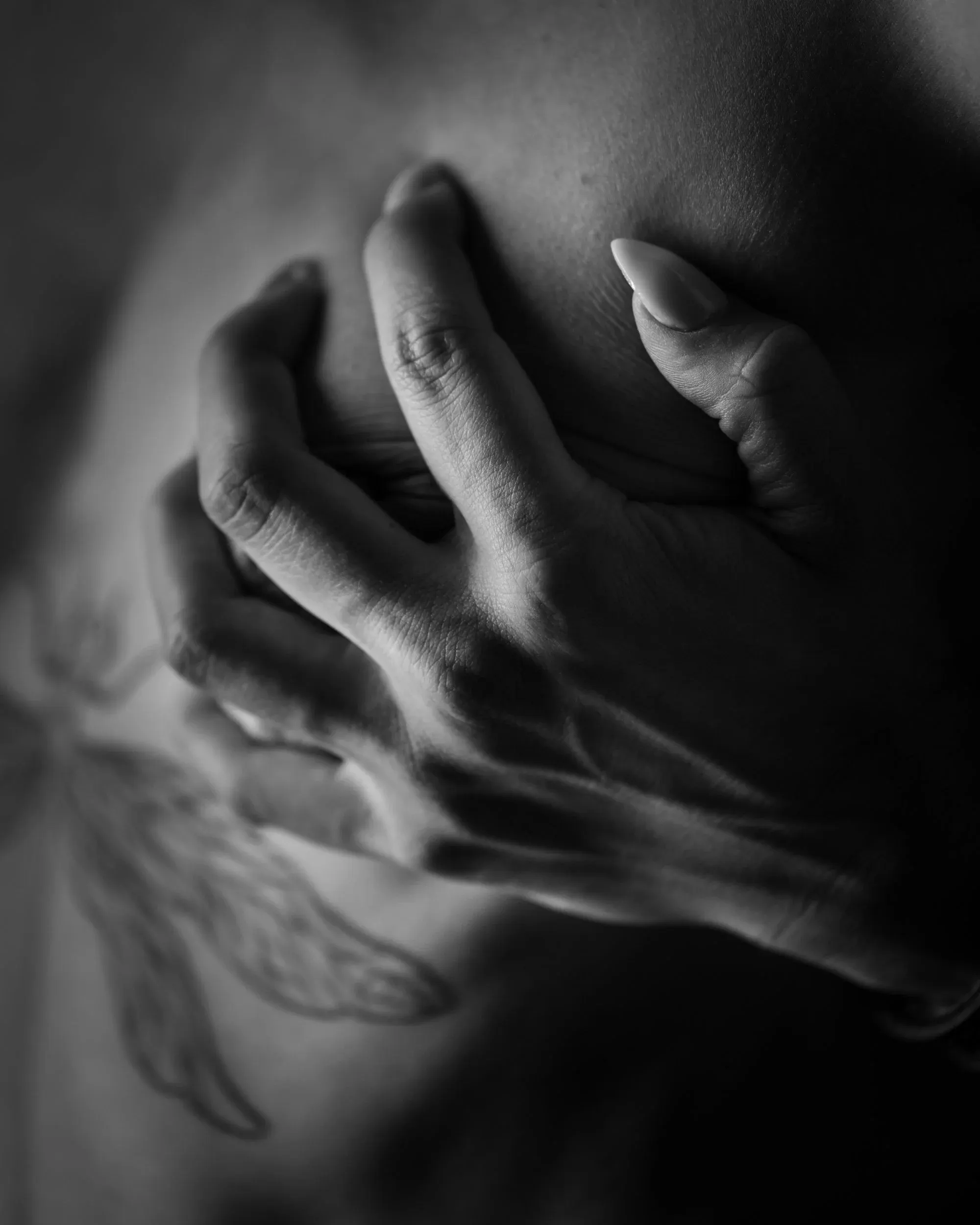 A hand presses into skin in a soft, shallow-focus close-up.