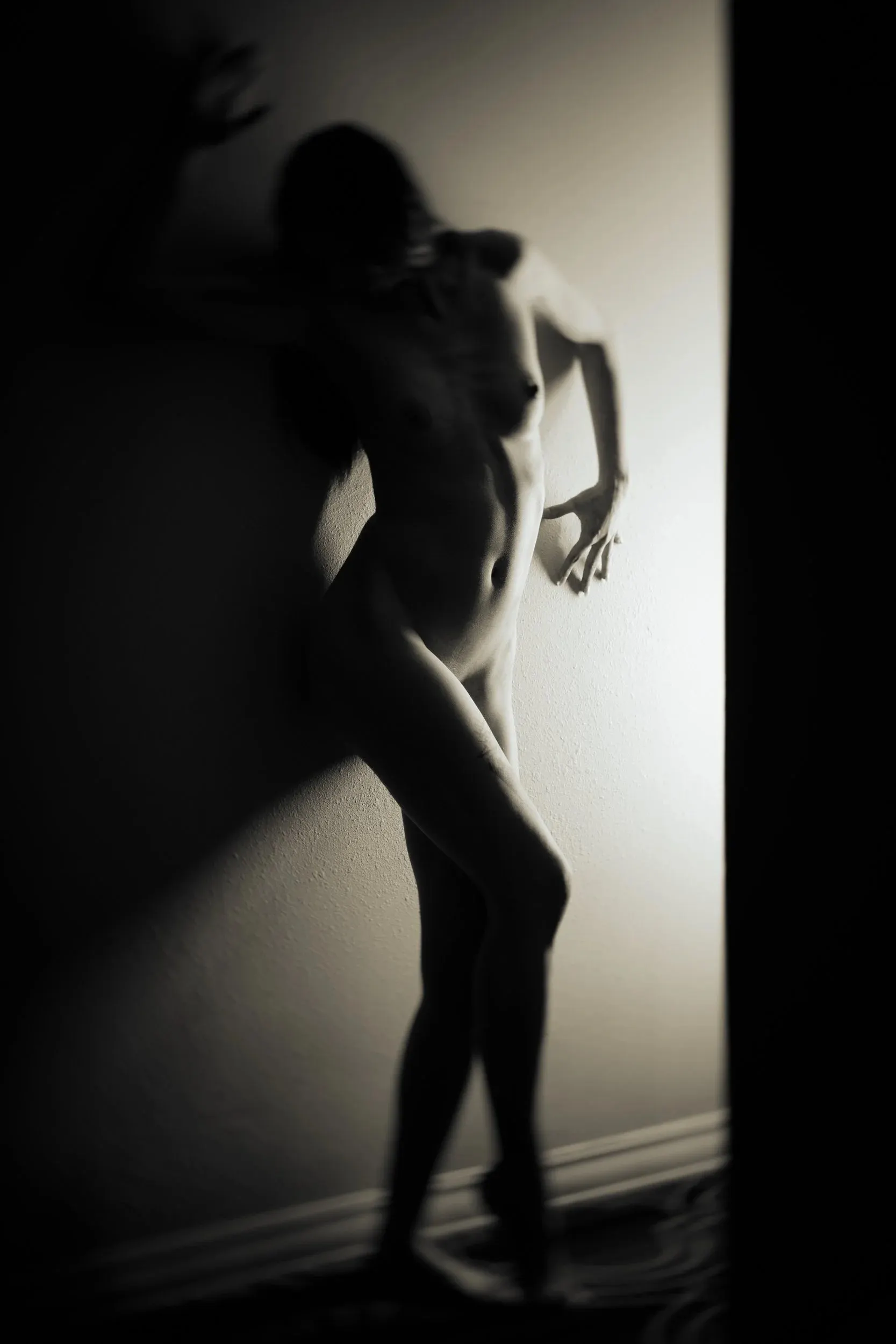 A standing figure casts a long angular shadow across a wall.