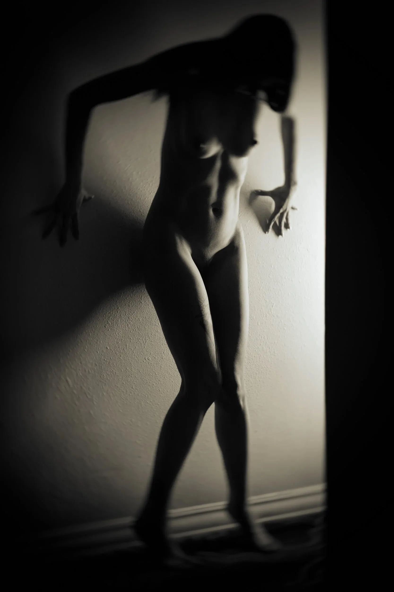 A woman leans into a wall as her shadow echoes the pose.