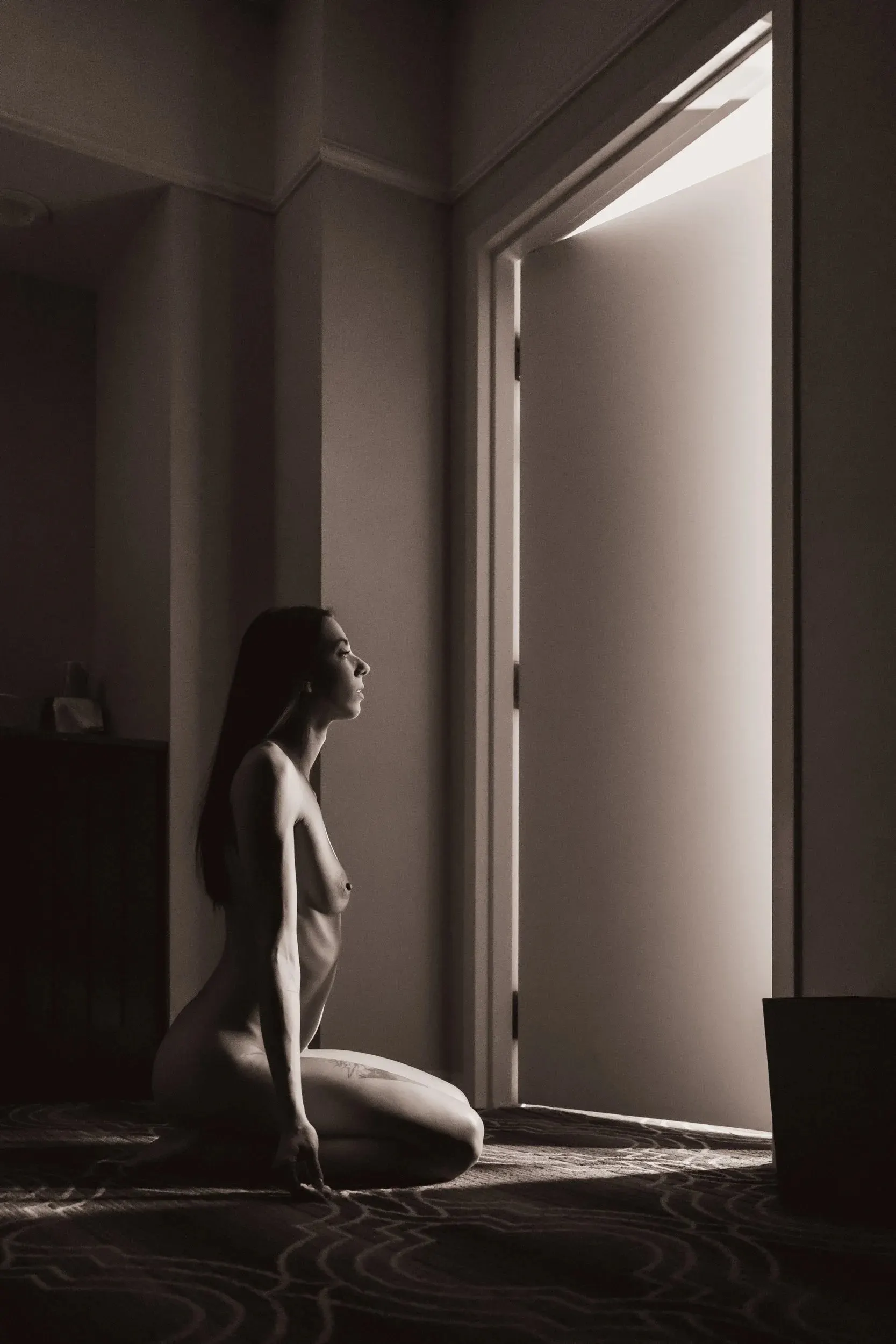 A kneeling silhouette waits beside an open, brightly lit door.