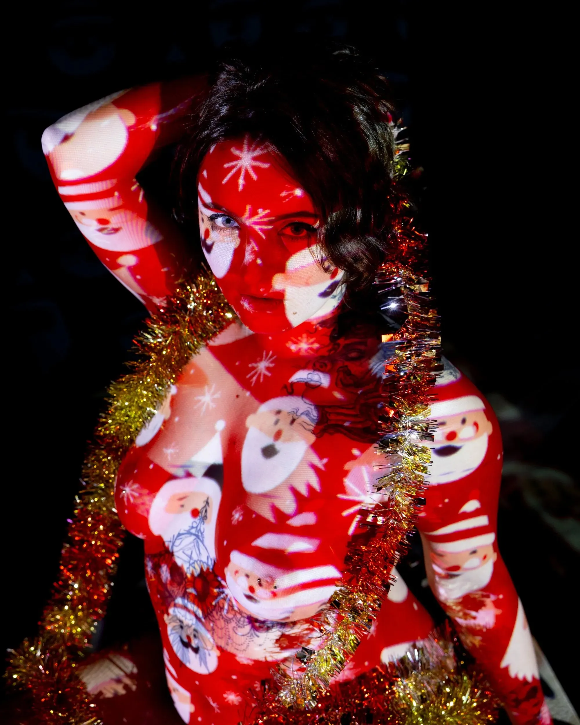 A woman wrapped in gold tinsel is covered by red Santa projection.