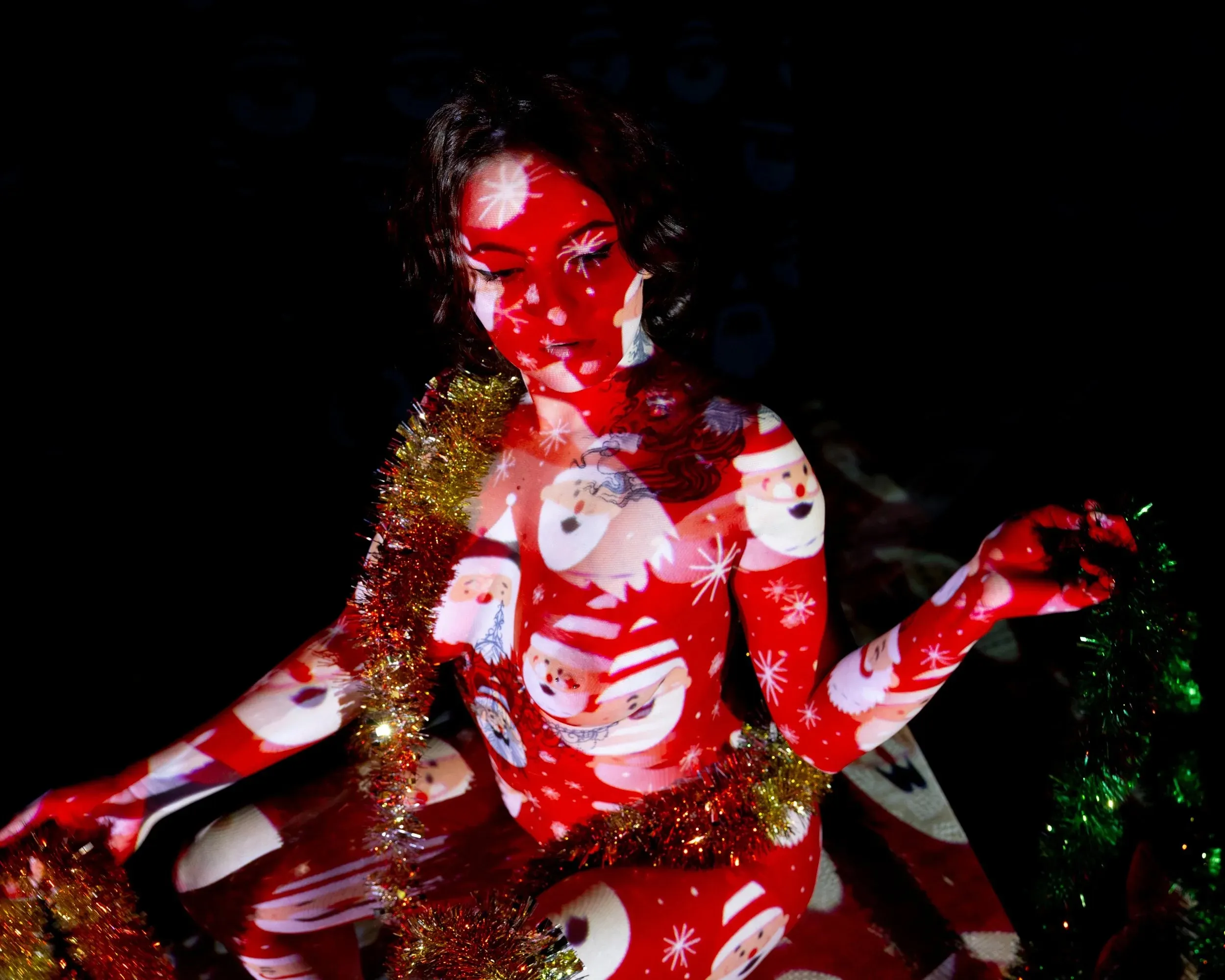 A seated woman gestures beside a gift box while red patterns cover the scene.