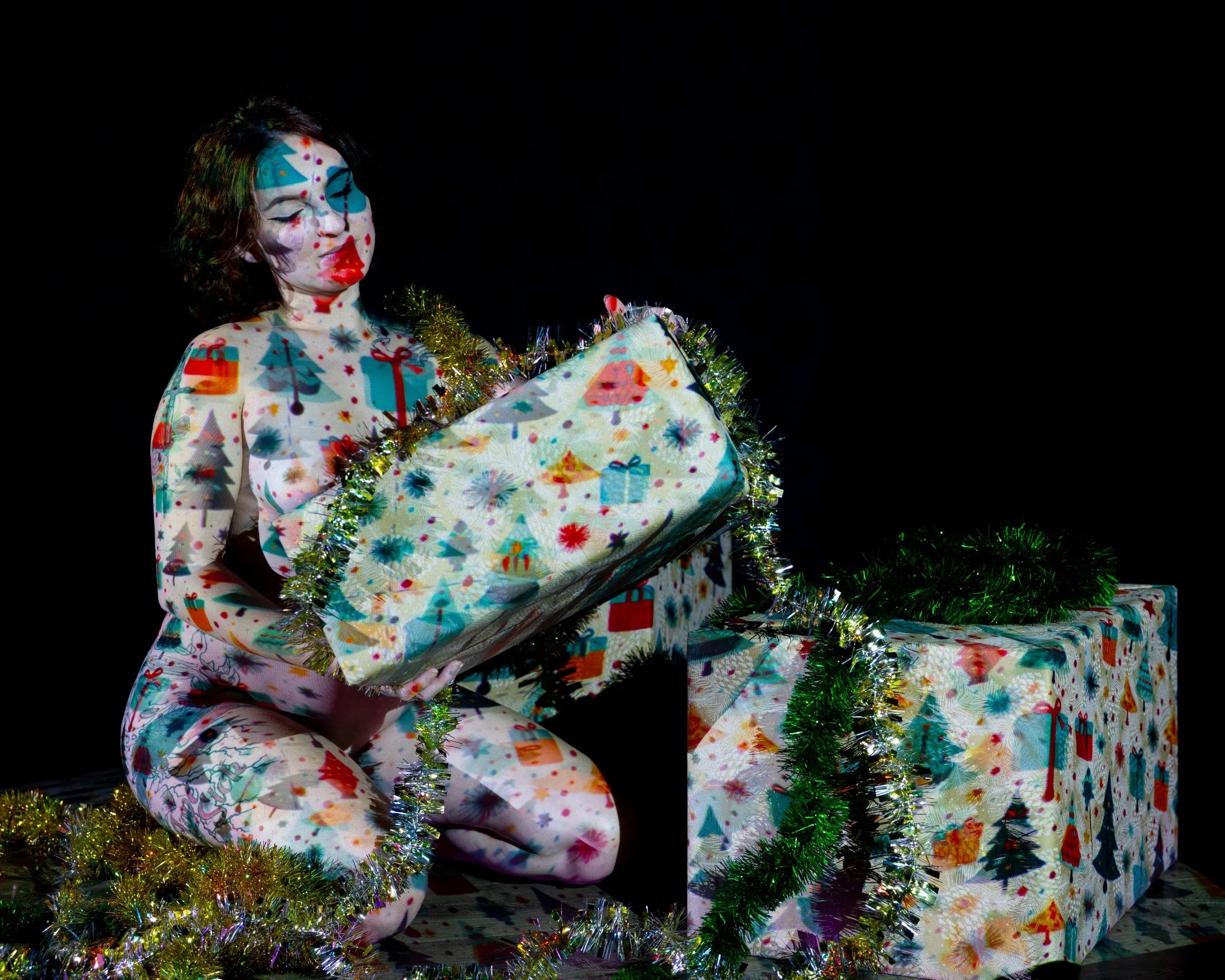 A seated woman lifts a patterned gift box under blue projection.