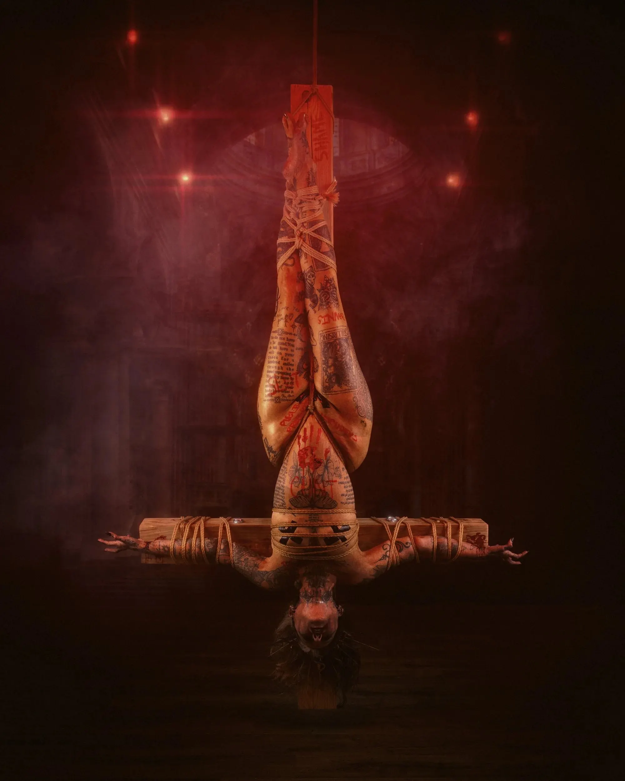An upside-down figure is bound to a wooden cross amid red haze and sparks.