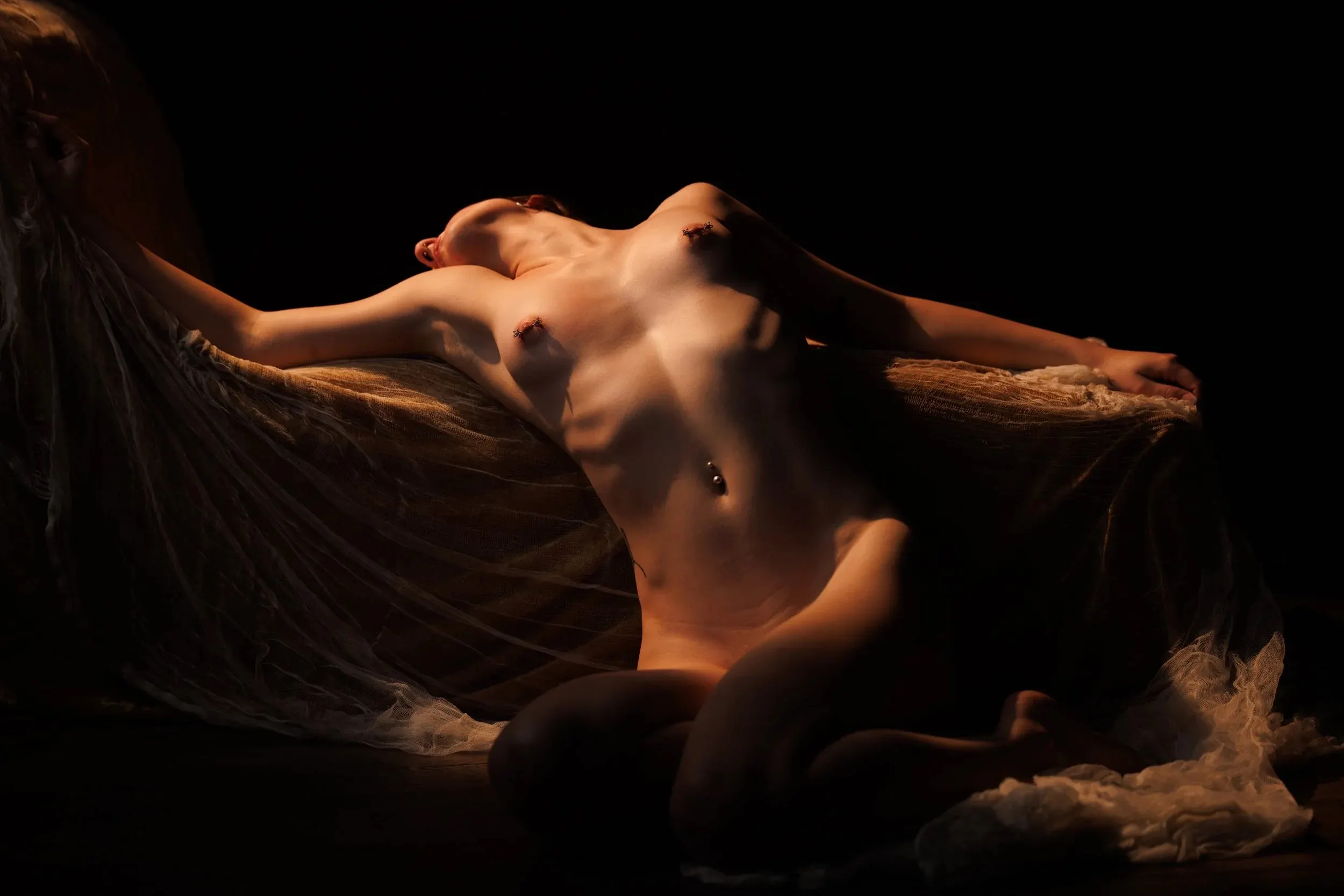 A woman stretches across dark fabric with her face tilted into warm light.