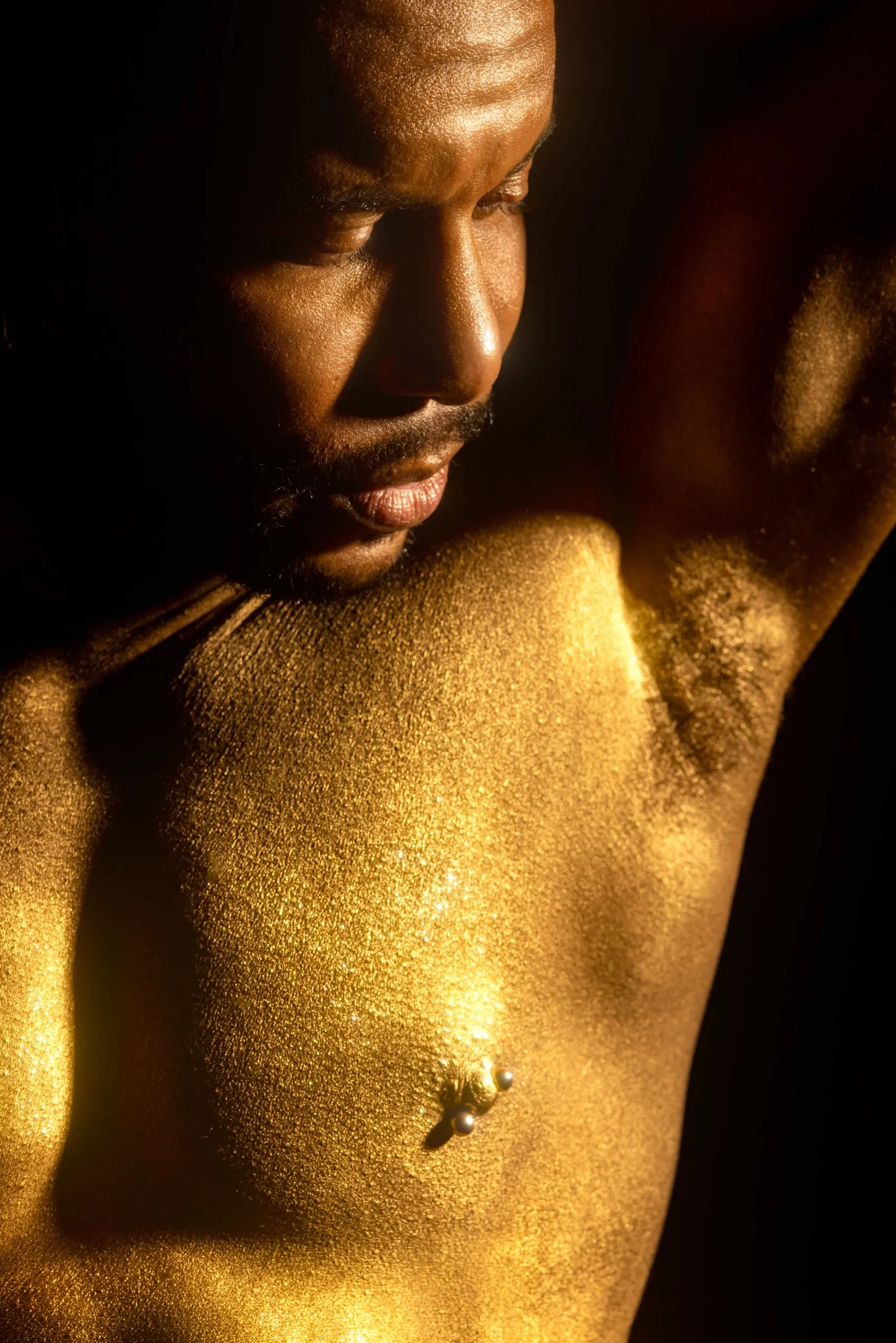 A gold-painted man looks downward with one arm raised.