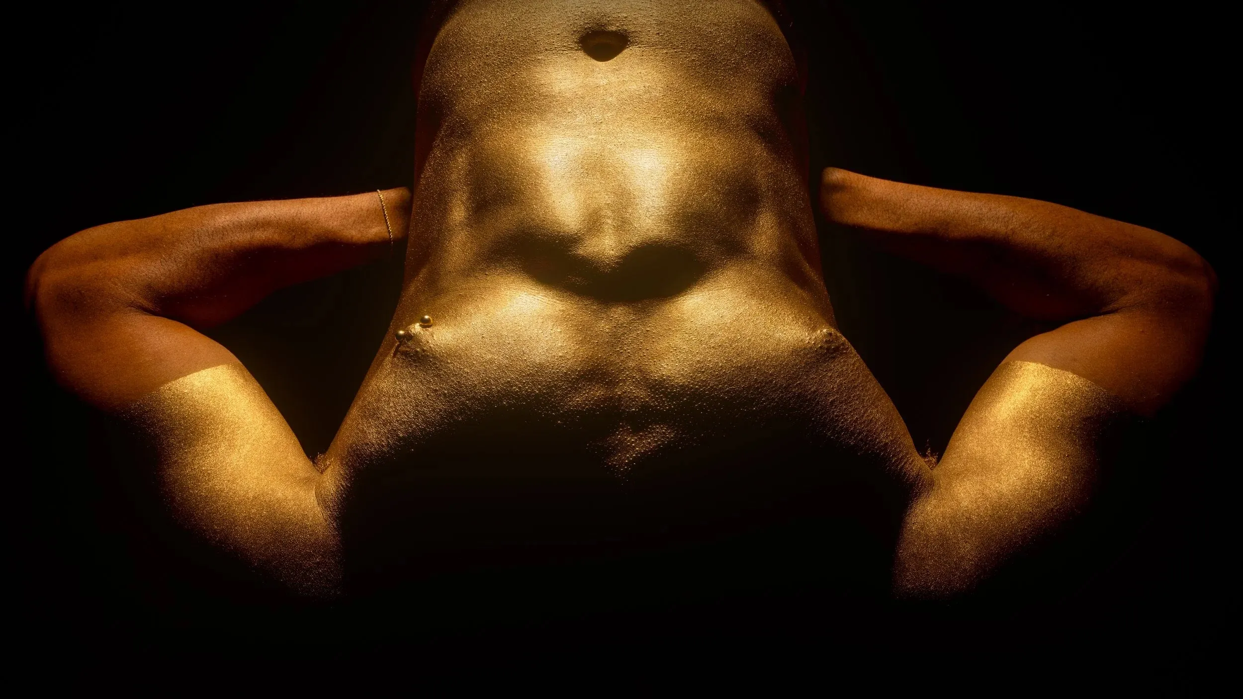 A low-angle view frames a gold-painted torso with arms extending outward.