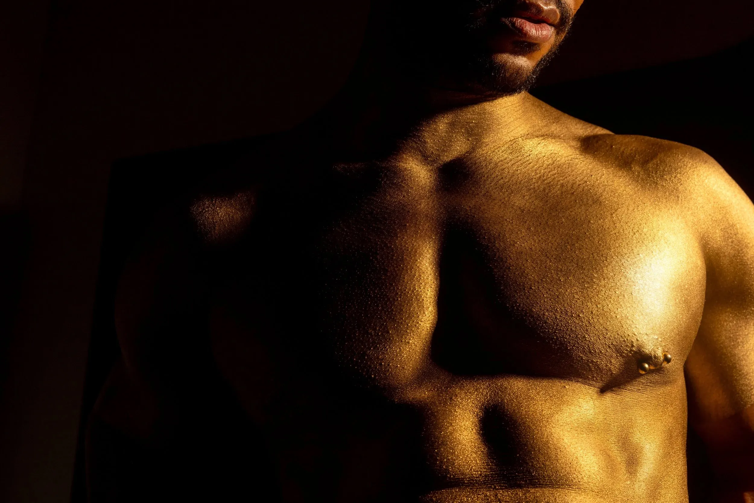 A gold-painted chest and shoulder emerge from a narrow column of light.
