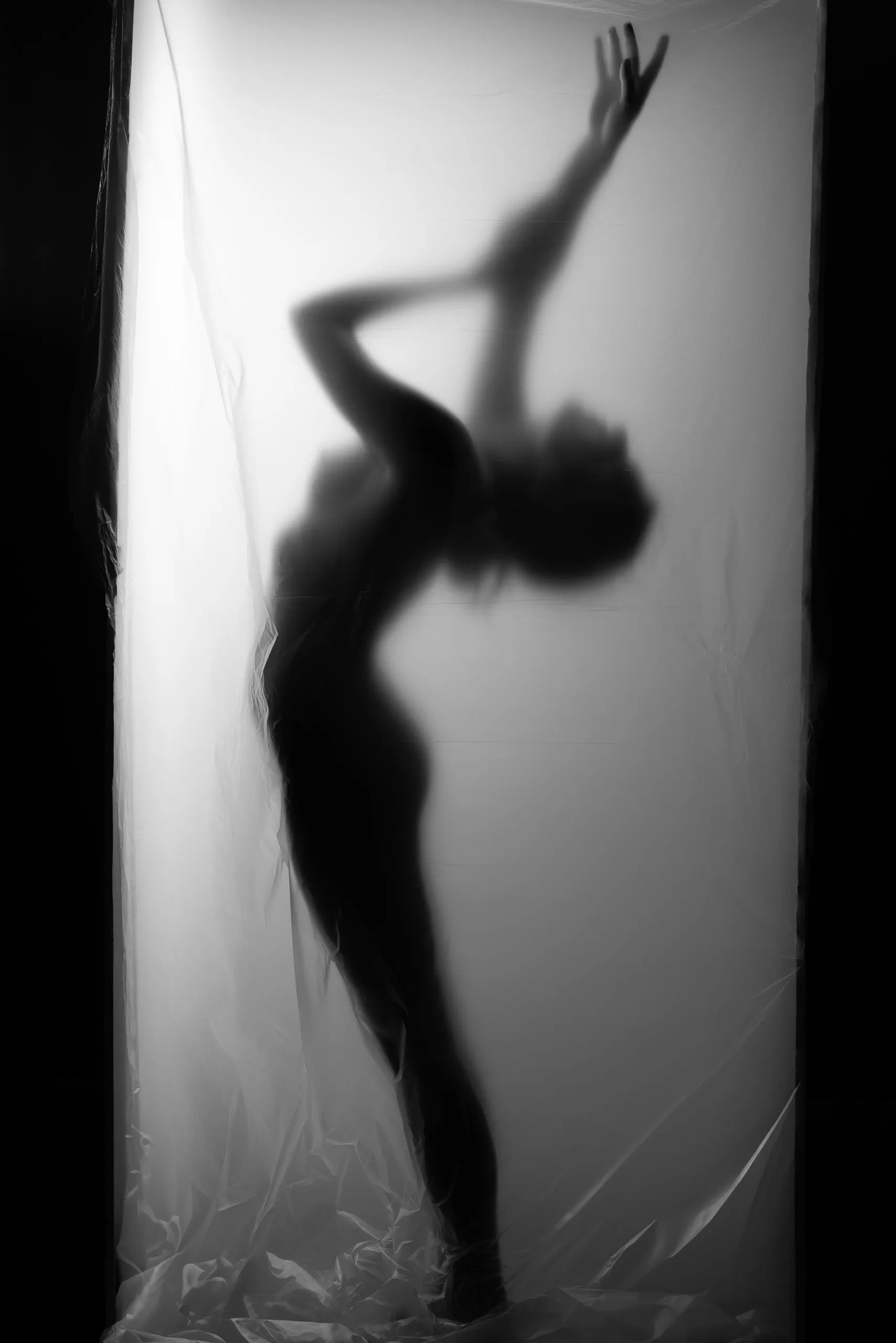 A blurred silhouette stretches behind a translucent curtain in black and white.