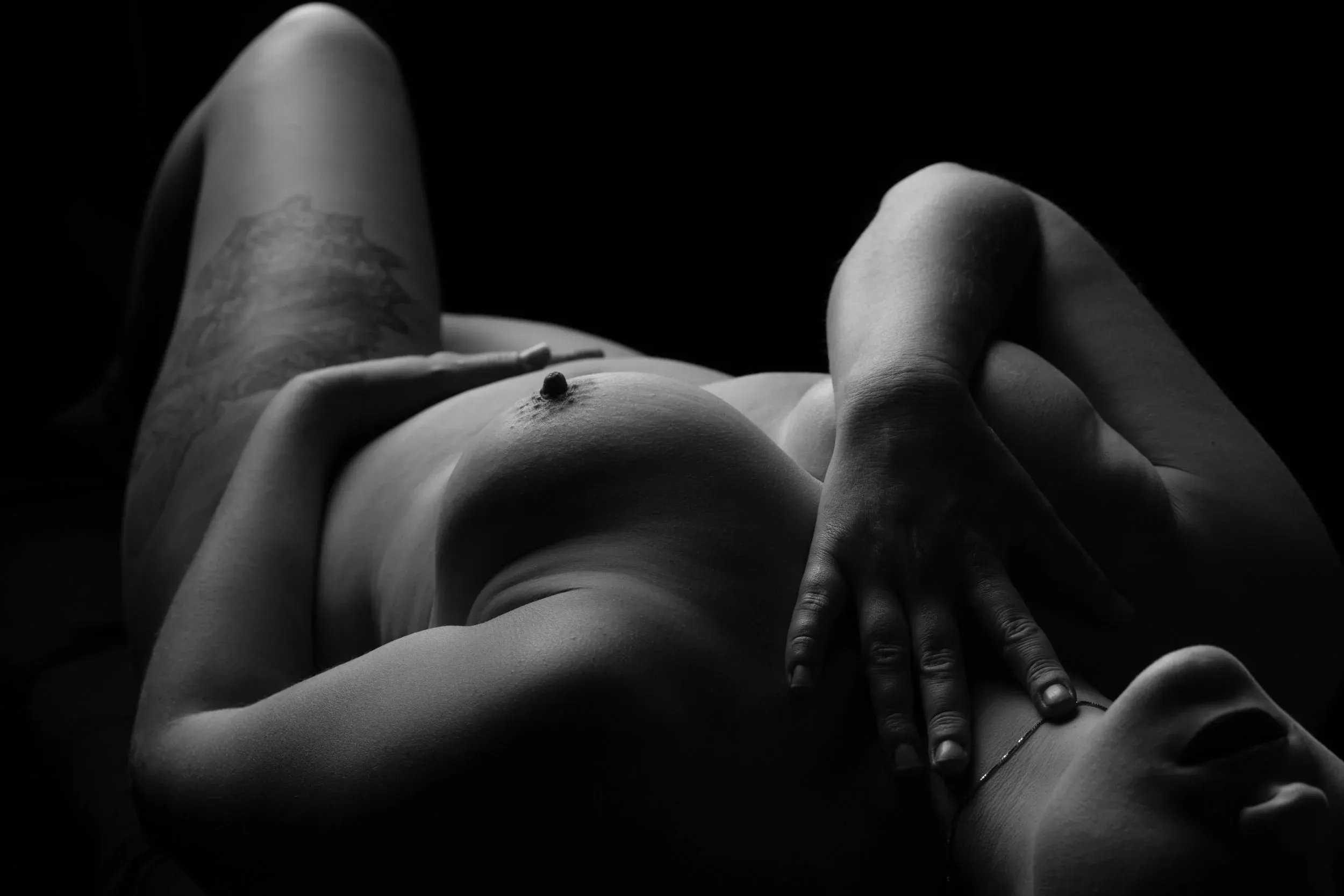 A nude woman lies on her back, lit from a single backlight.