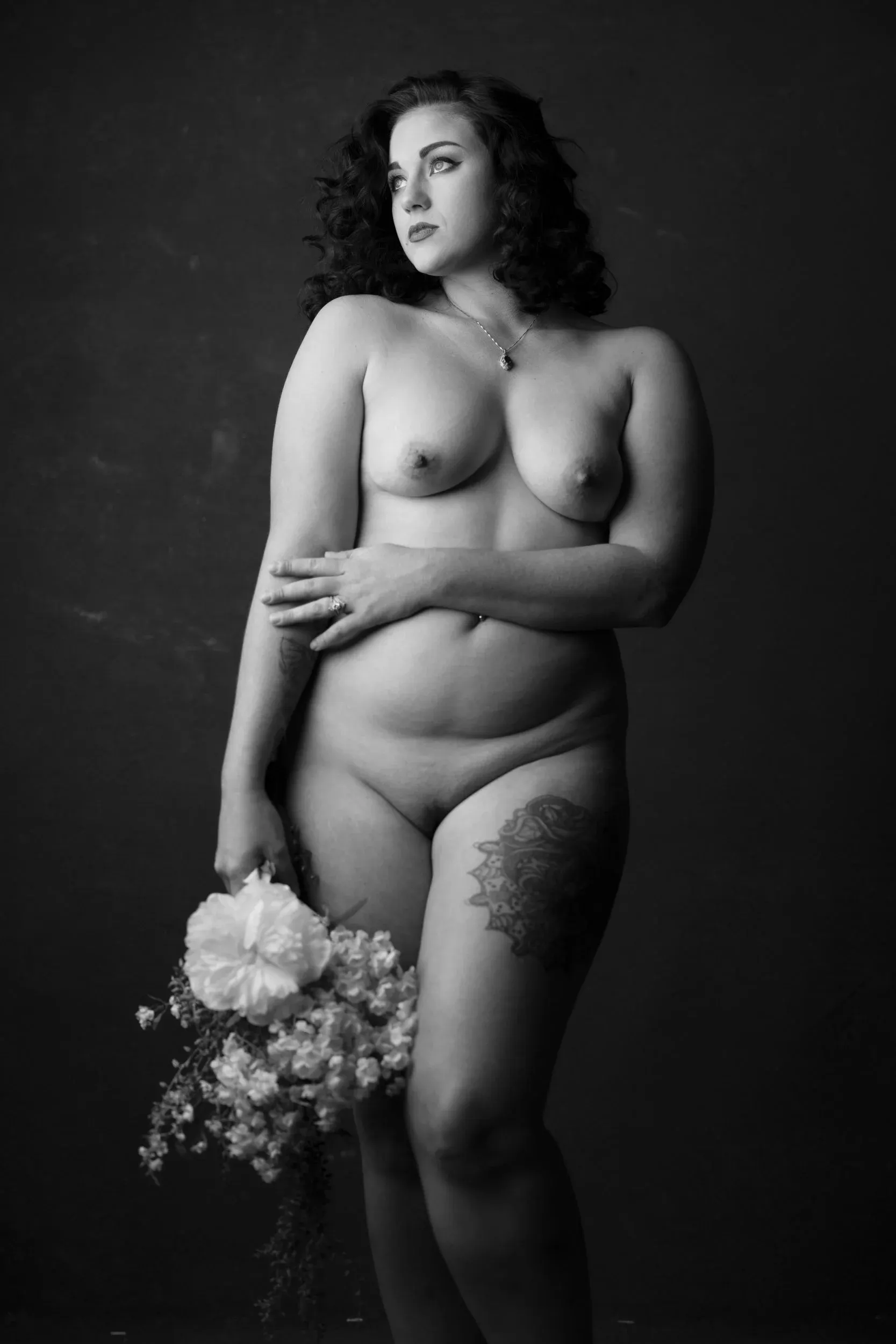 A woman crosses one arm while holding flowers at her side.