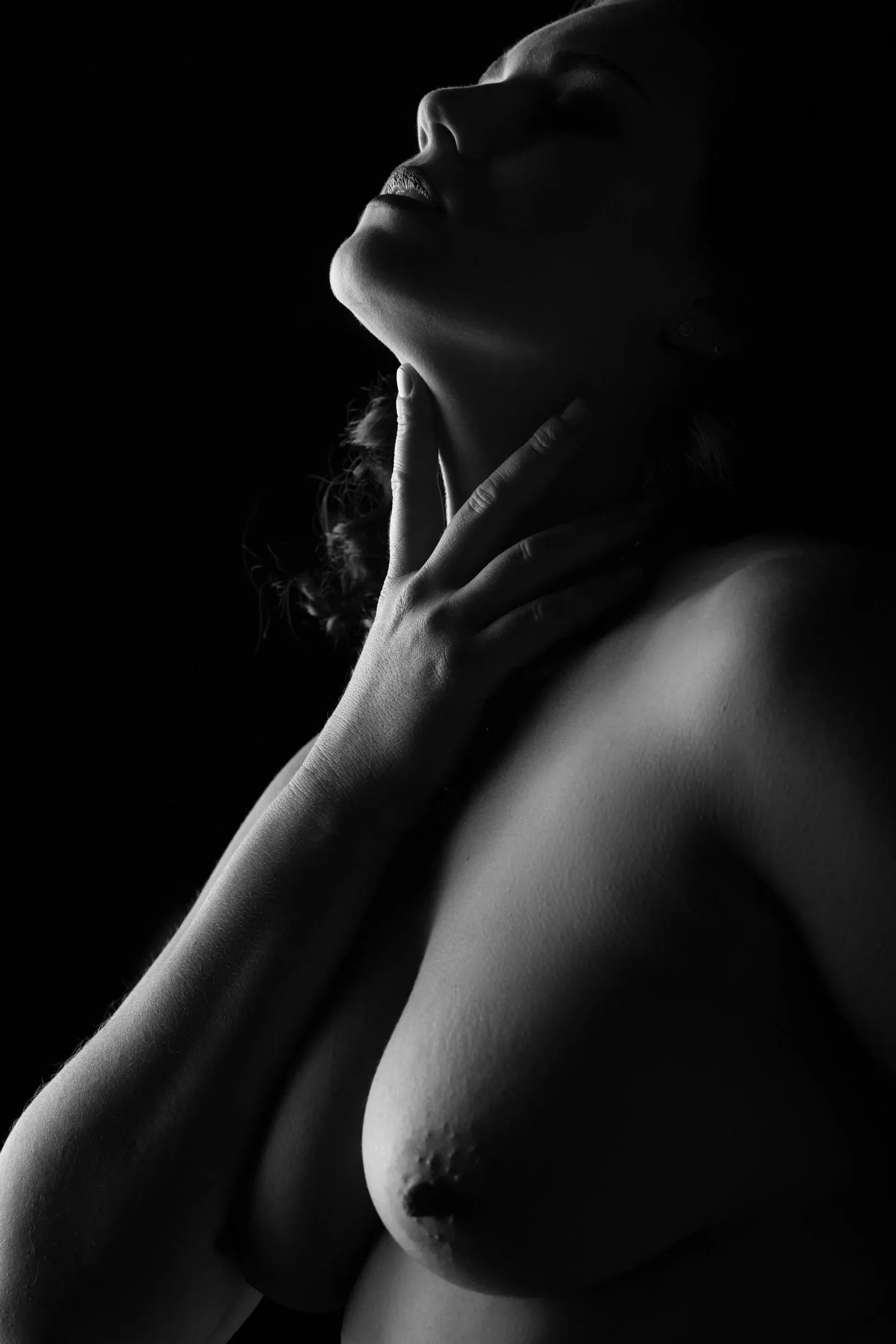 A close profile lifts her face and hands into a narrow edge of light.
