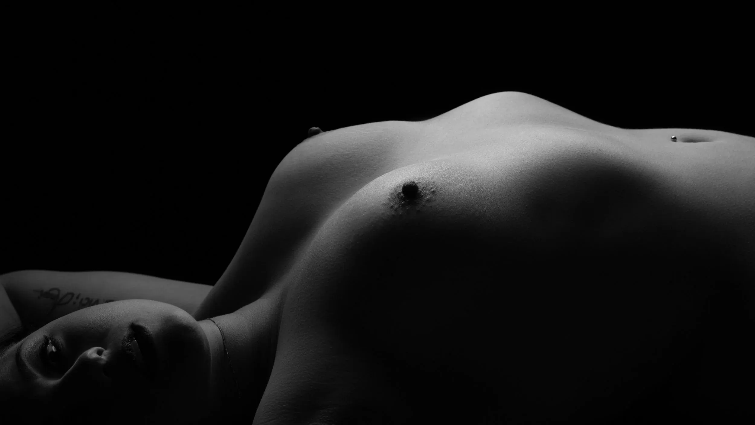 A reclining figure becomes a long wave of silver light against black.
