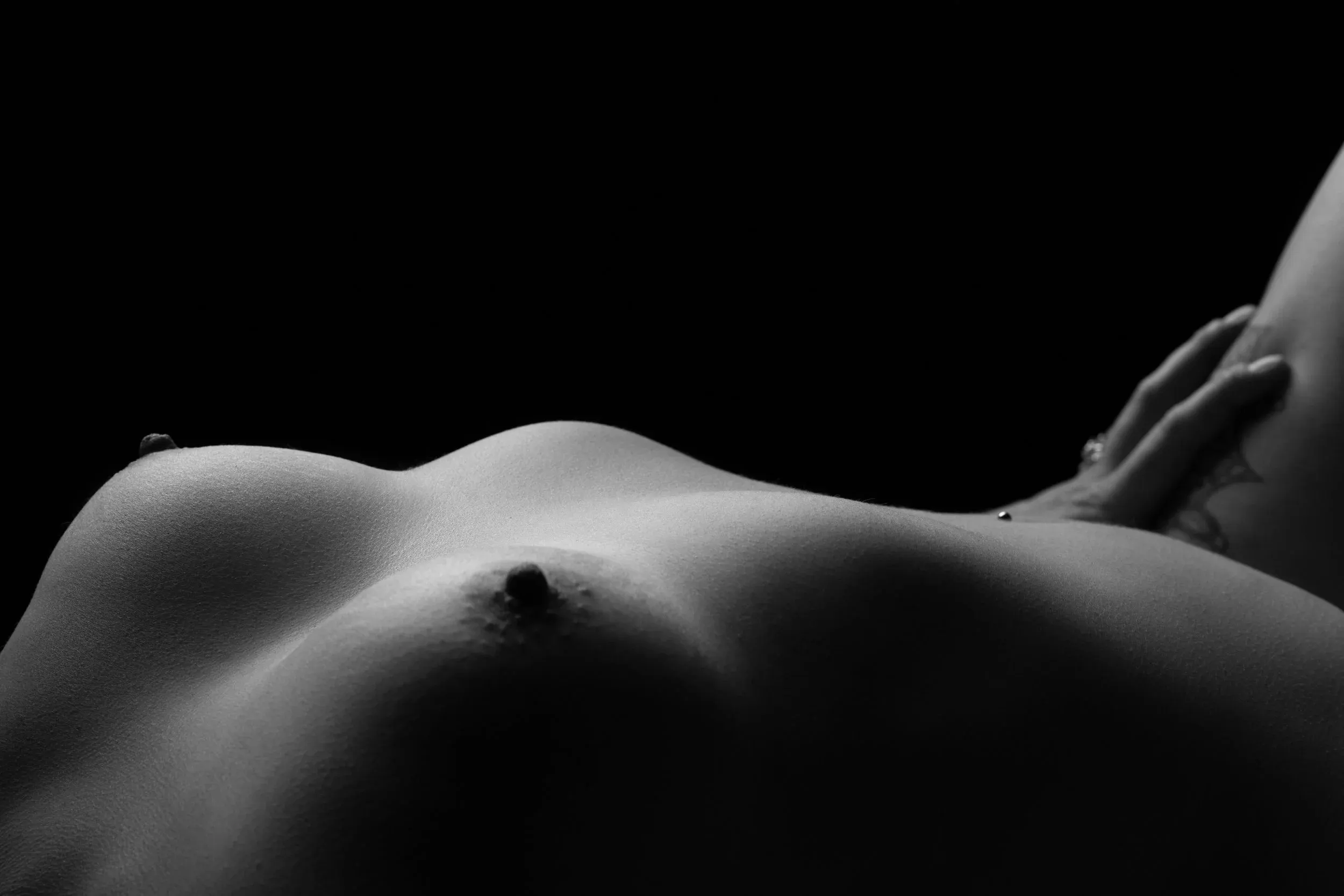 A hand rests on a reclining torso in a quiet horizontal study.