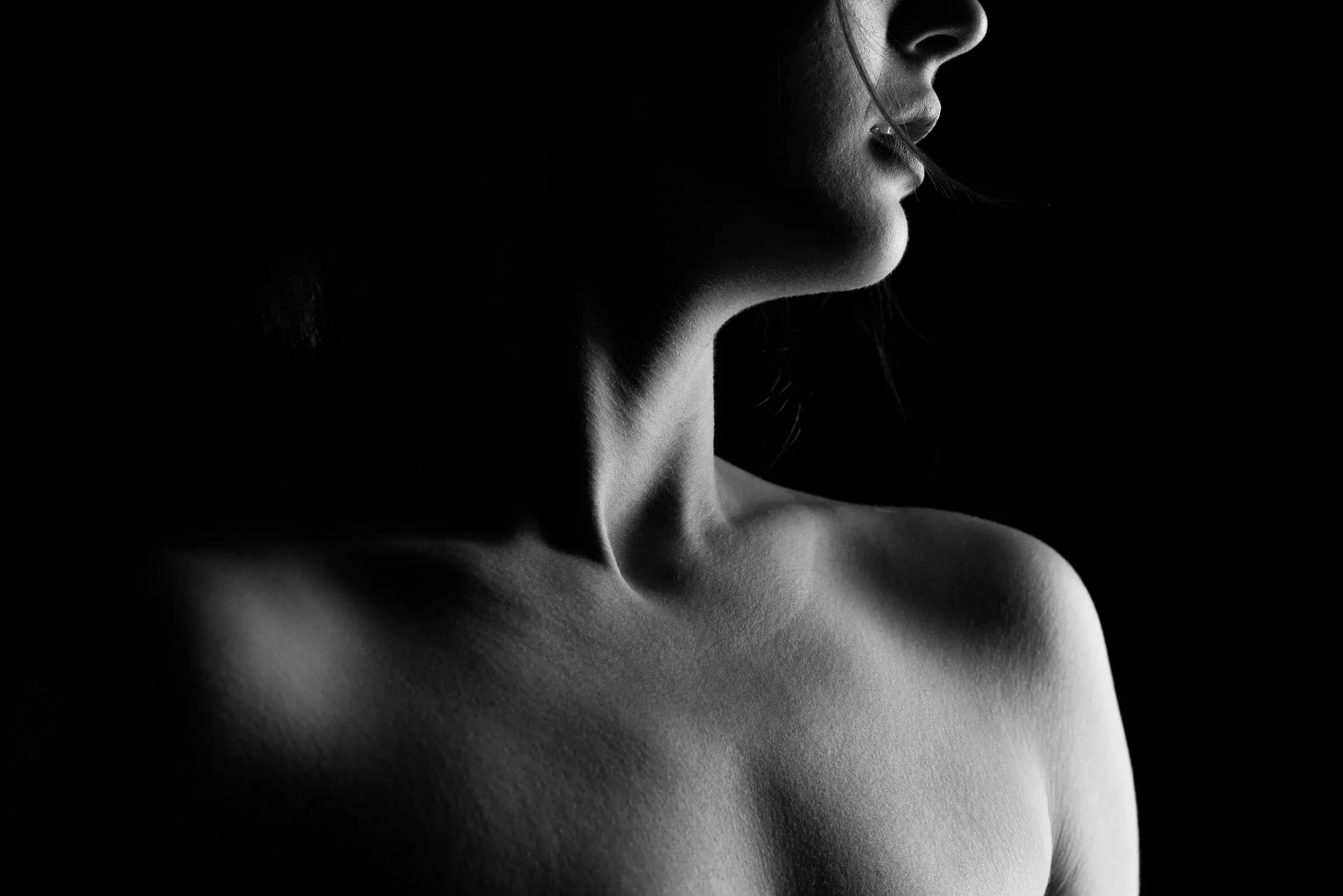 A close profile of chin, neck, and shoulders emerges from black.