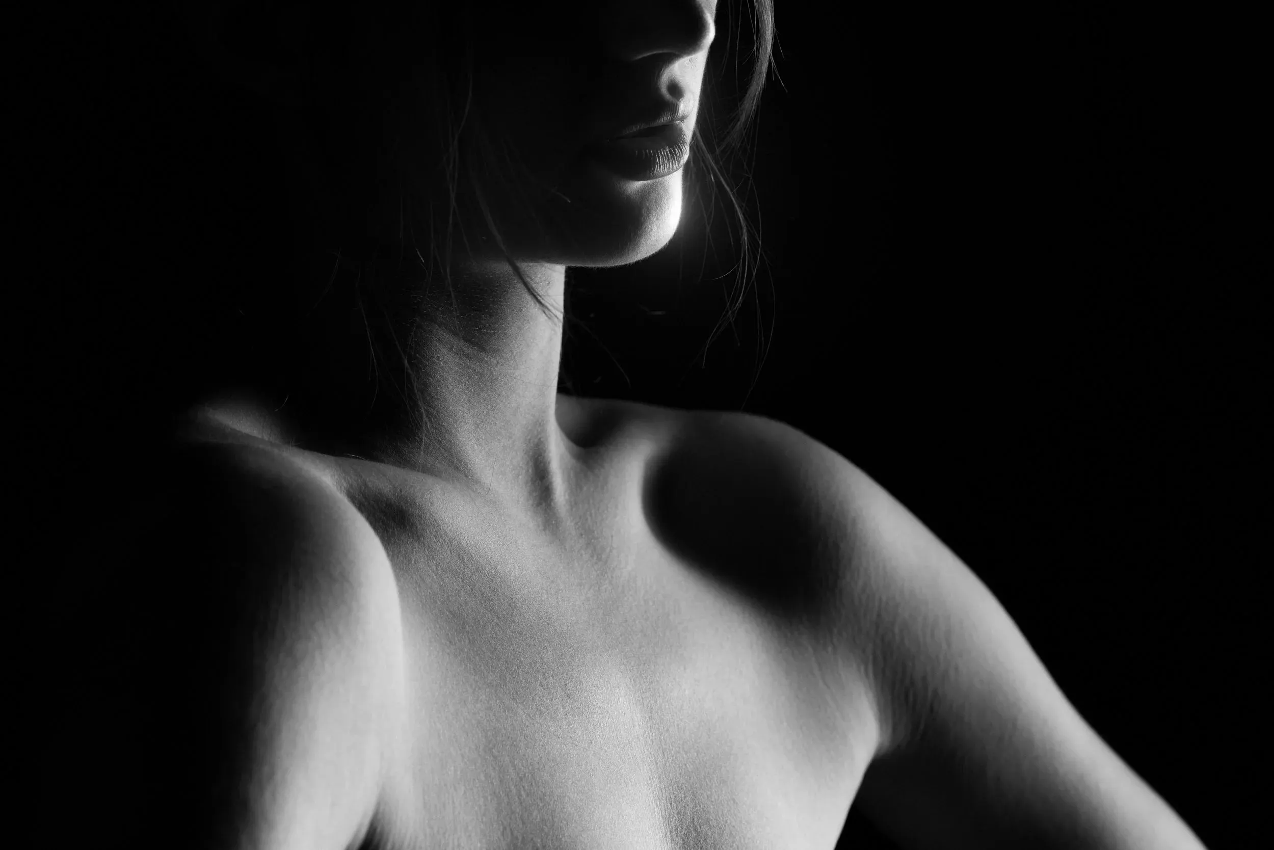 A close portrait isolates a shoulder and lower face in soft edge light.
