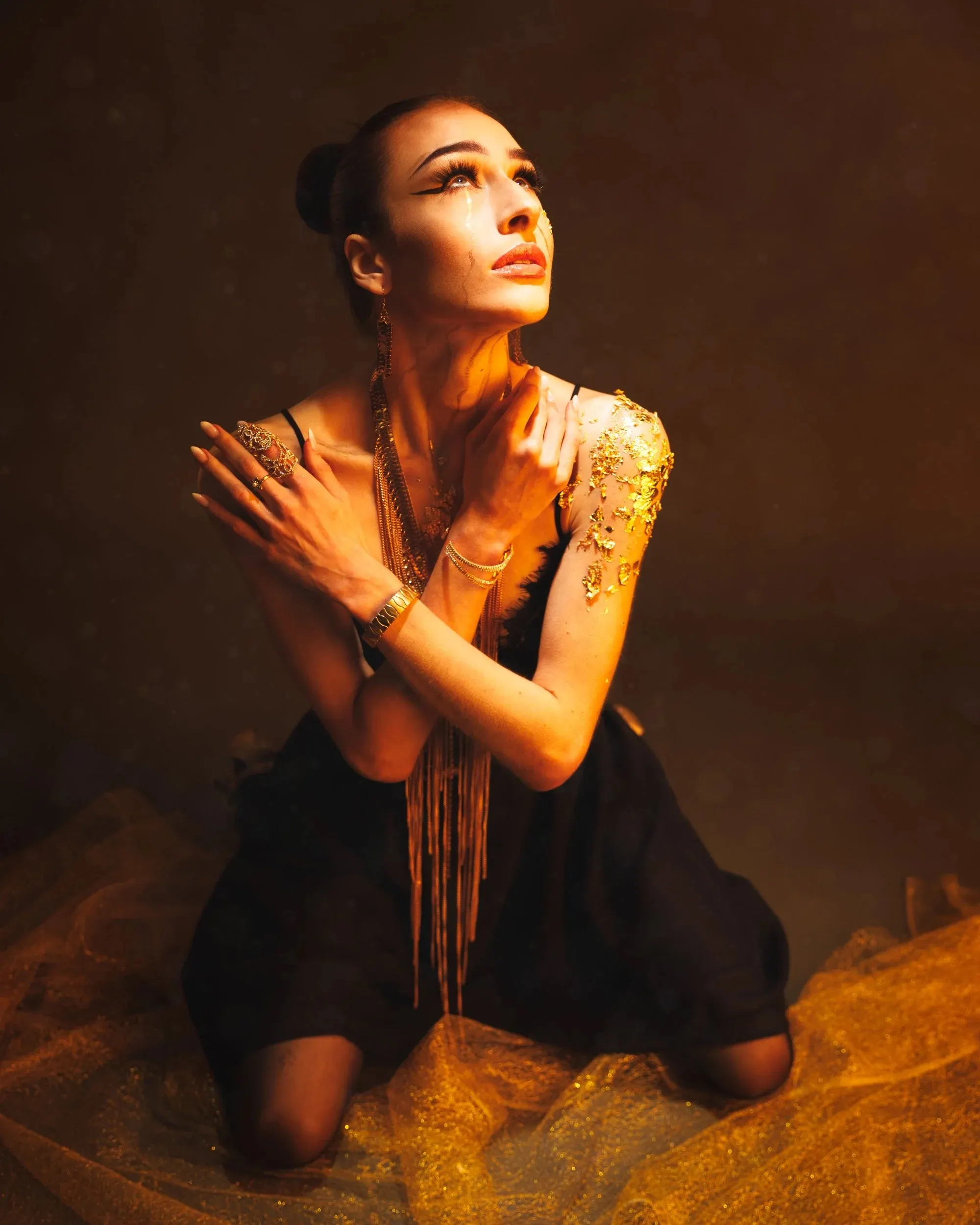 A kneeling woman in black looks upward through warm smoky light.