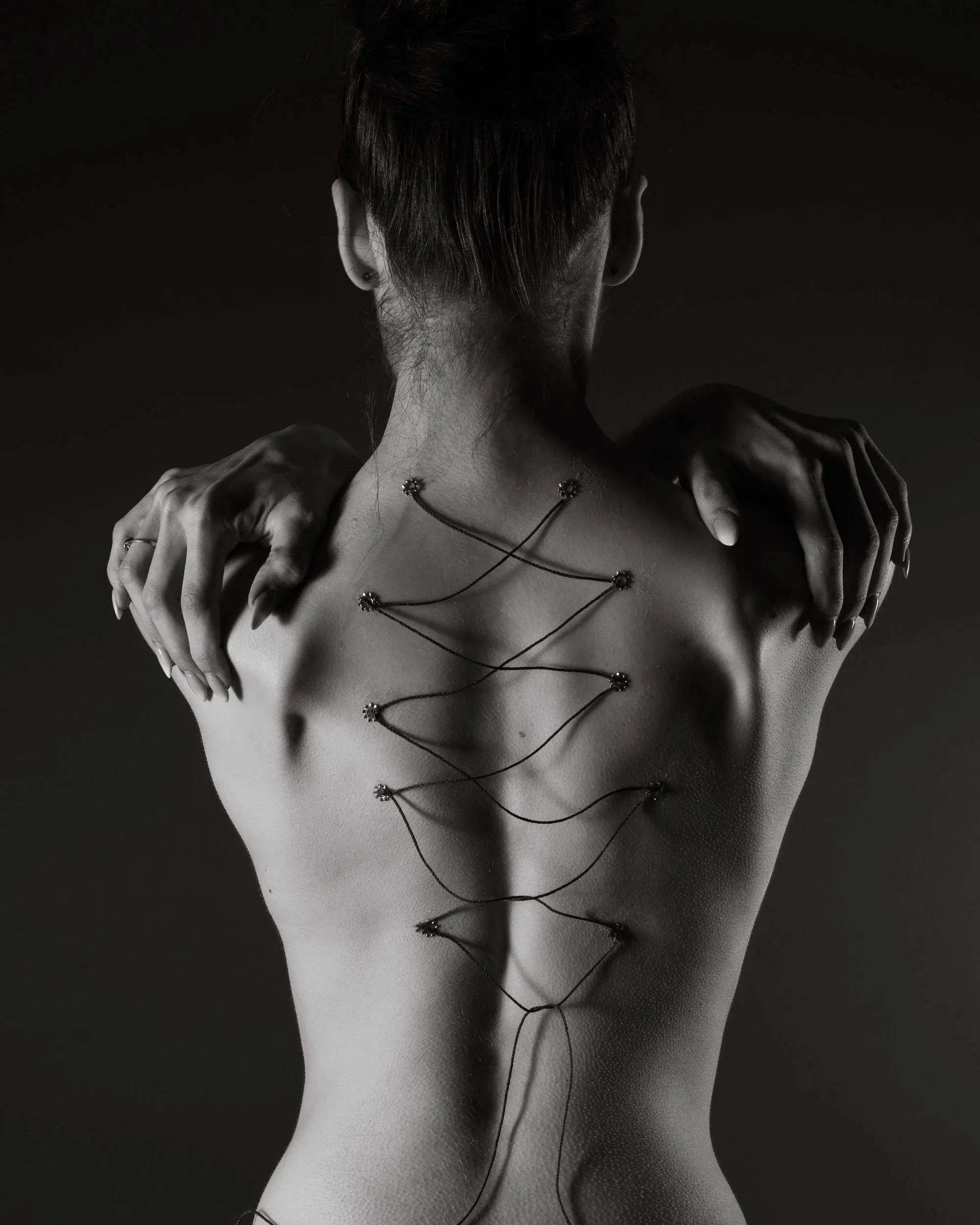 Black string forms a loose zigzag down a woman’s back in monochrome light.