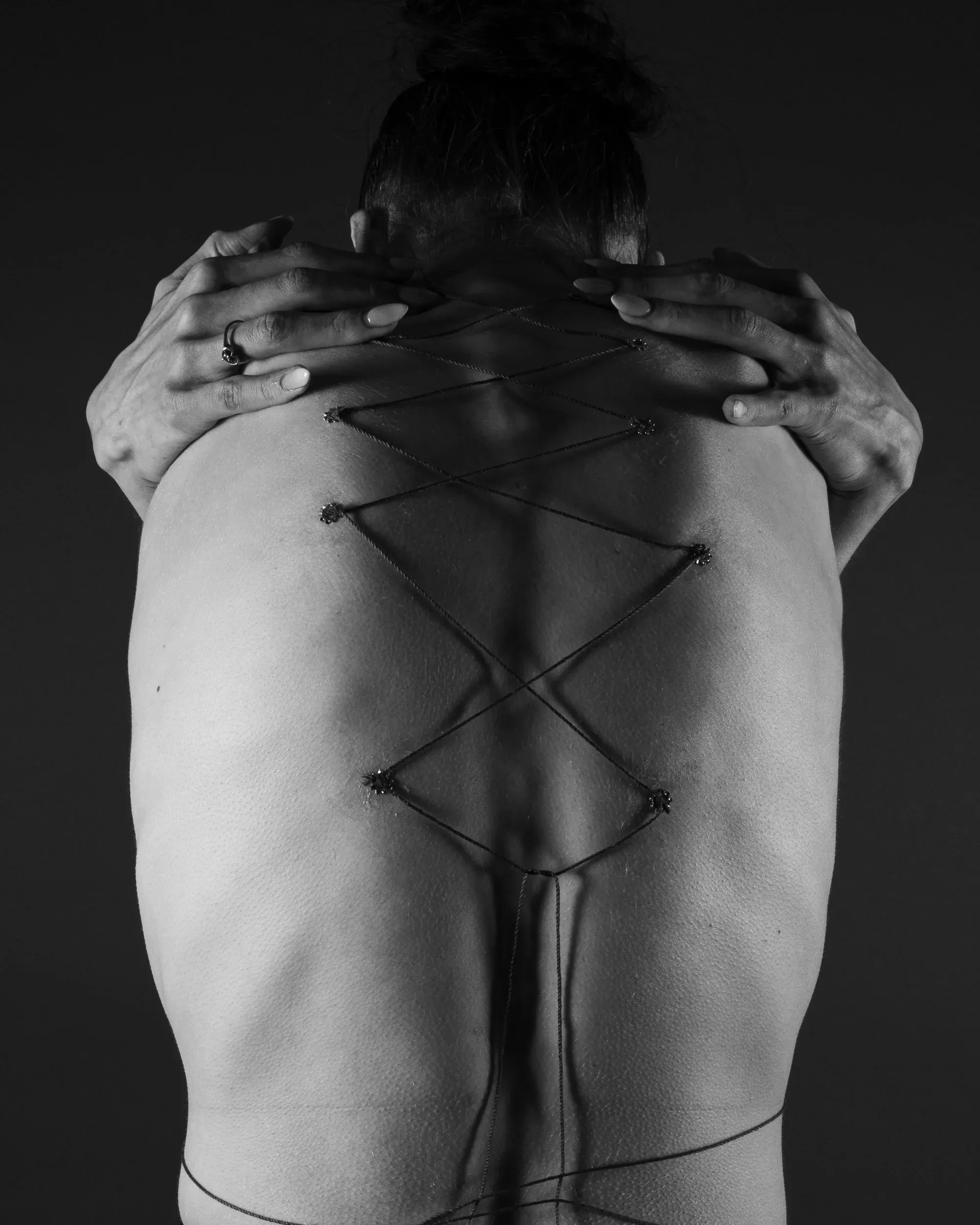 Hands and black string cross a close black-and-white view of a back.