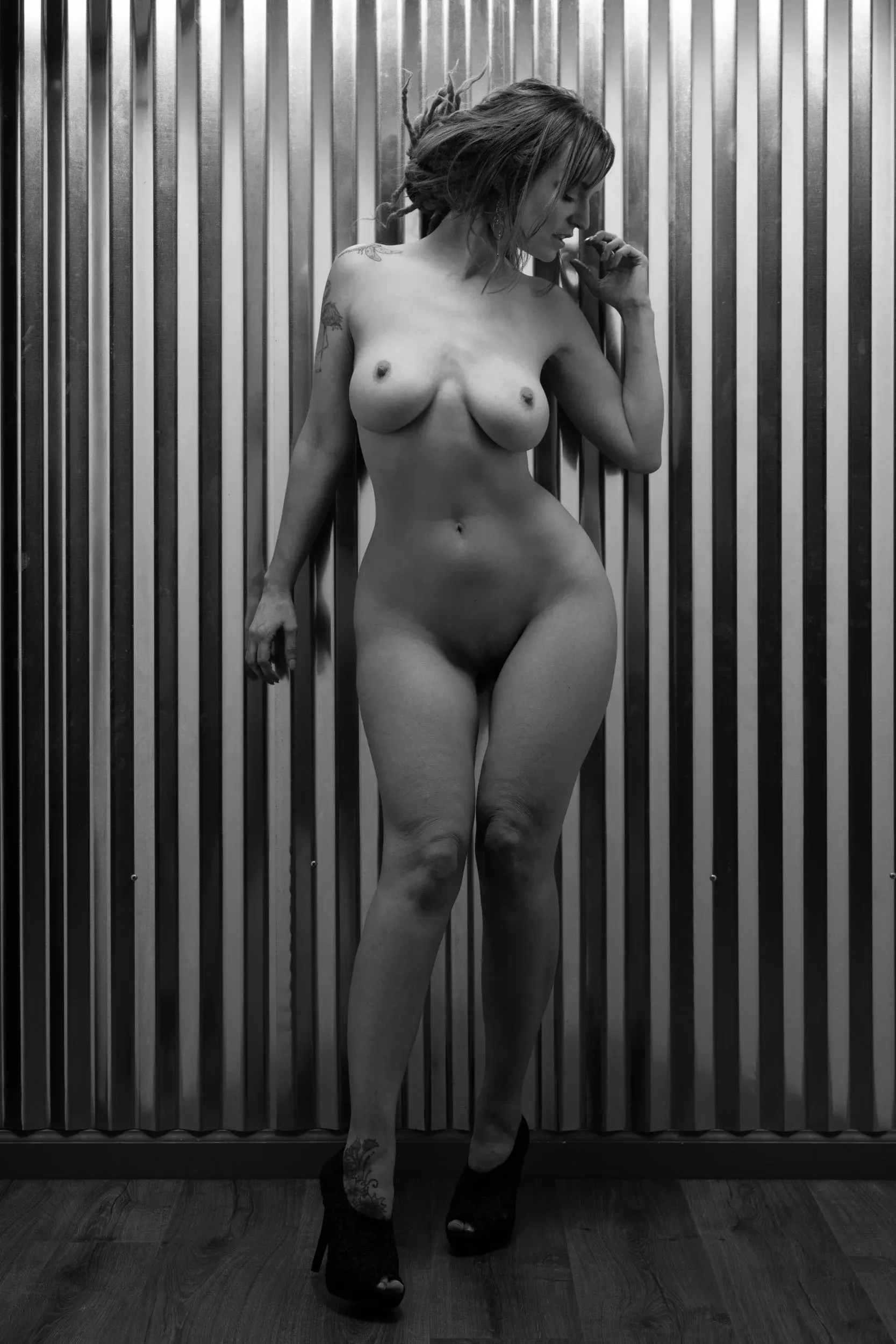 A woman in heels stands before corrugated metal in black and white.