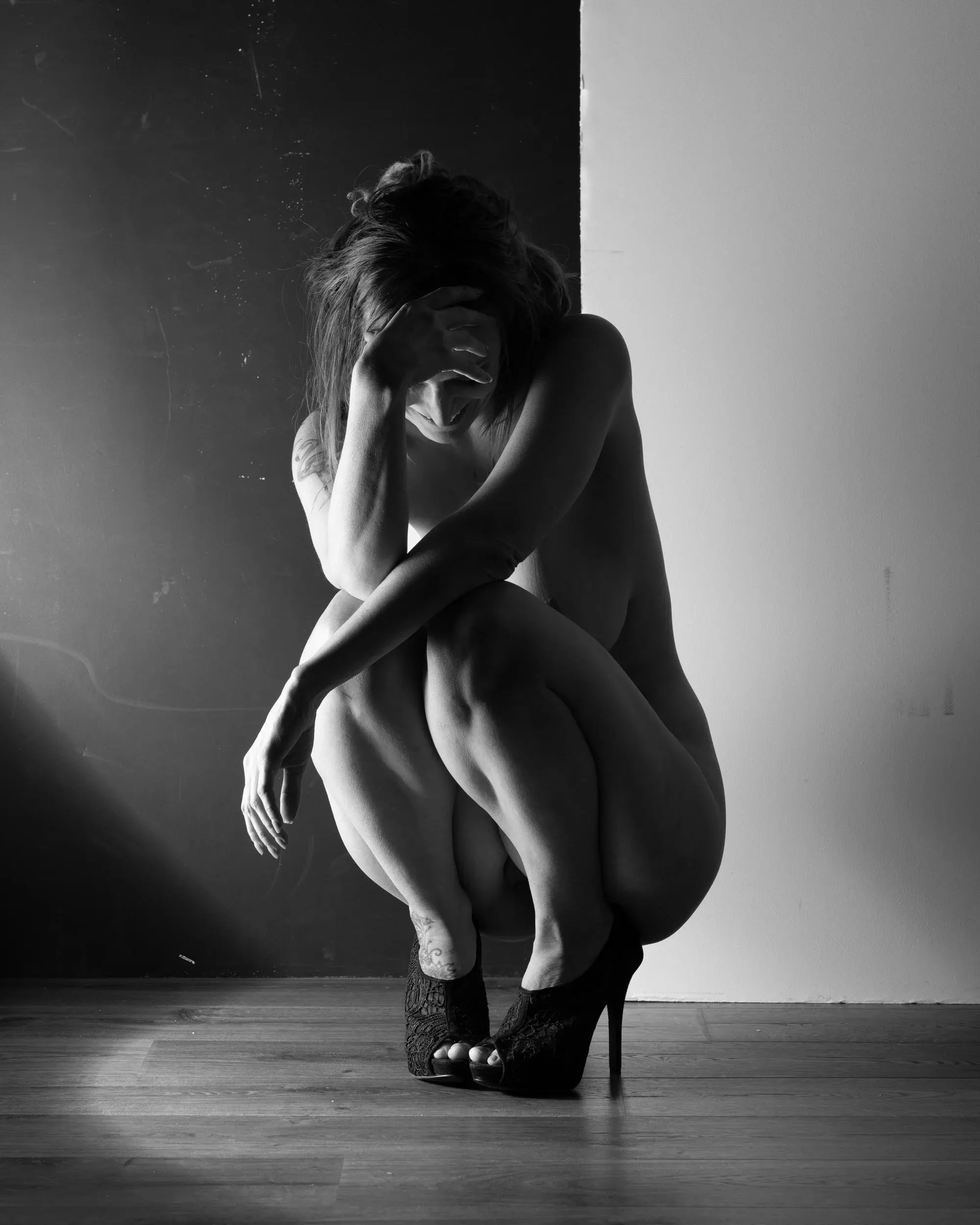 A crouching figure bows her head into a stark black-and-white shadow.