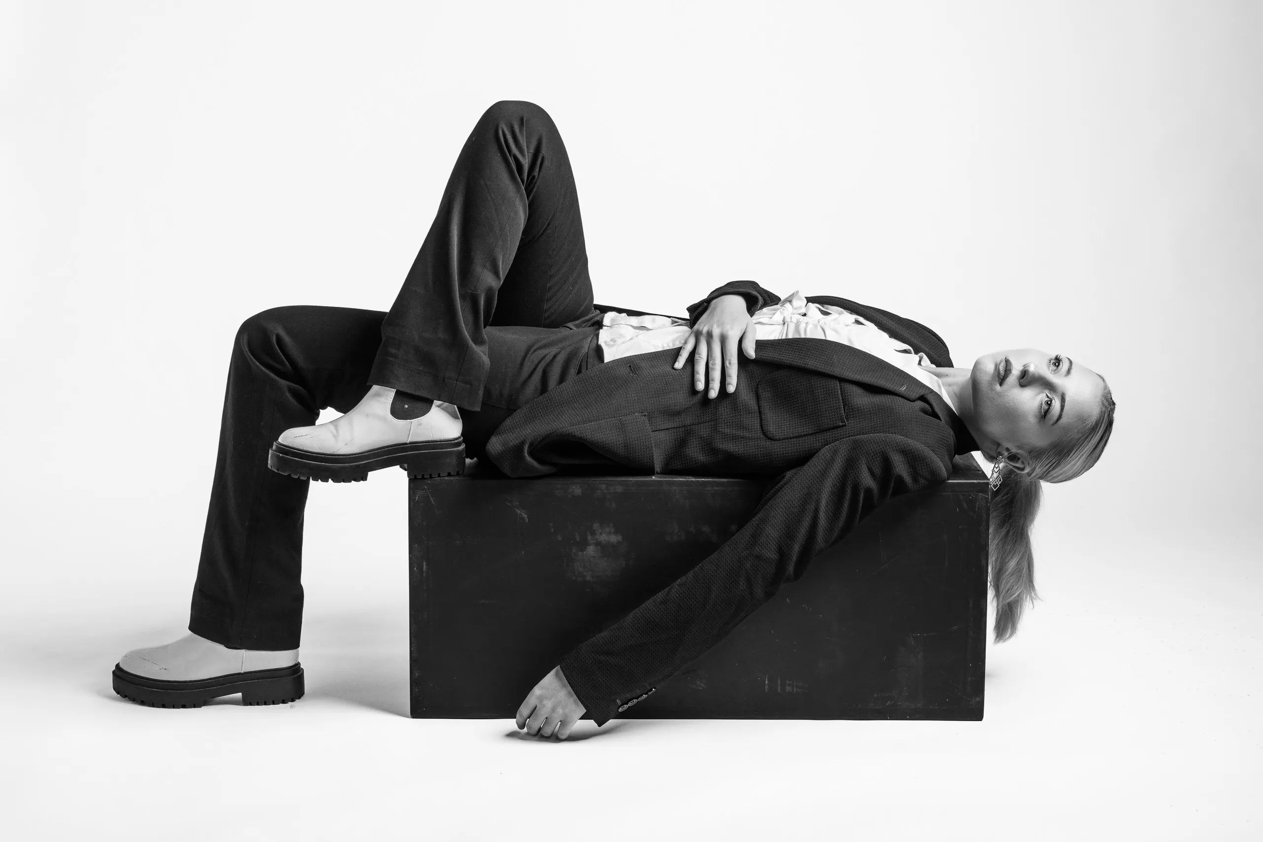 A person wearing a suit and white shoes lying on a black box.