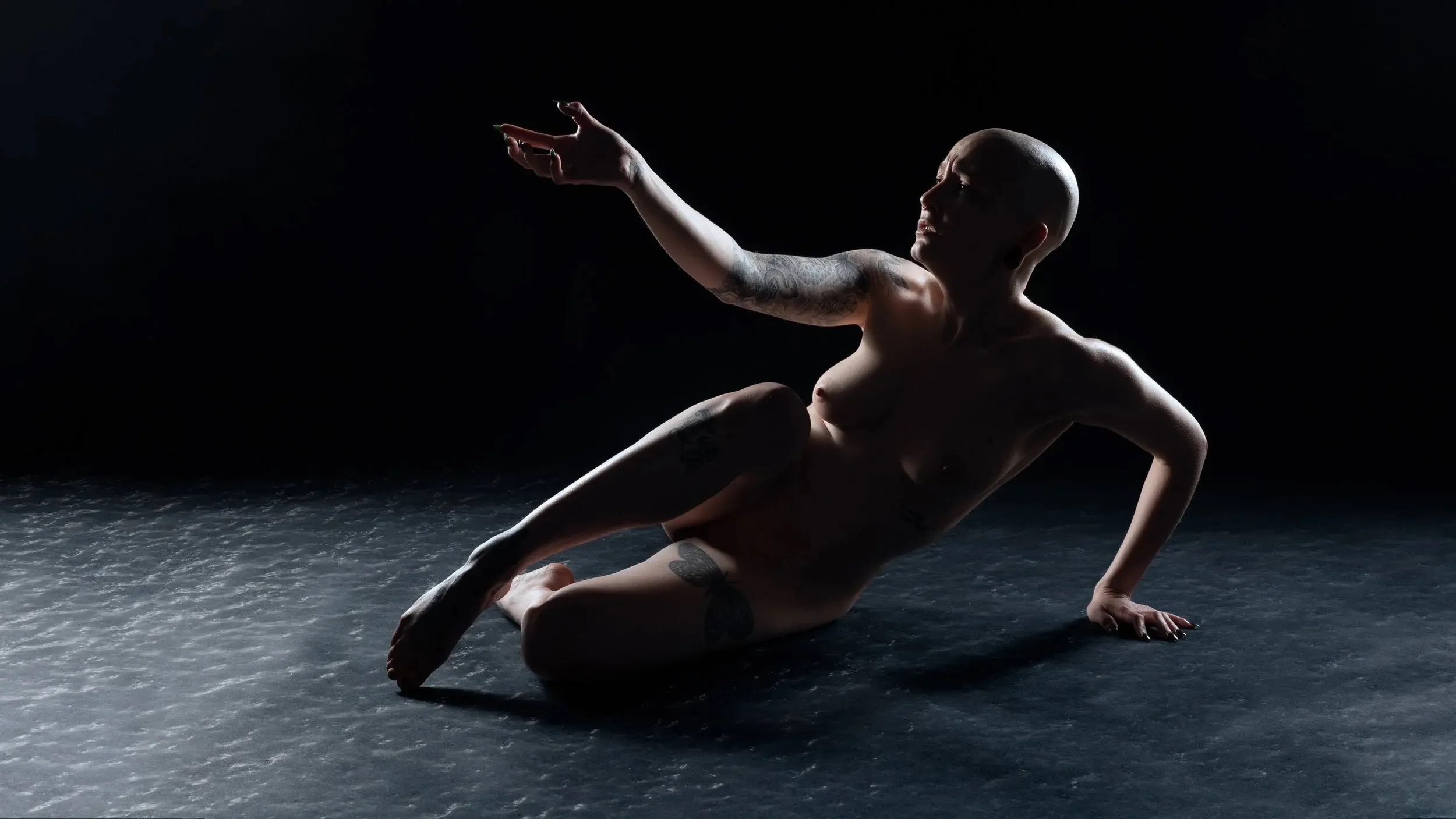 A reclining figure reaches outward across an icy blue floor against black.